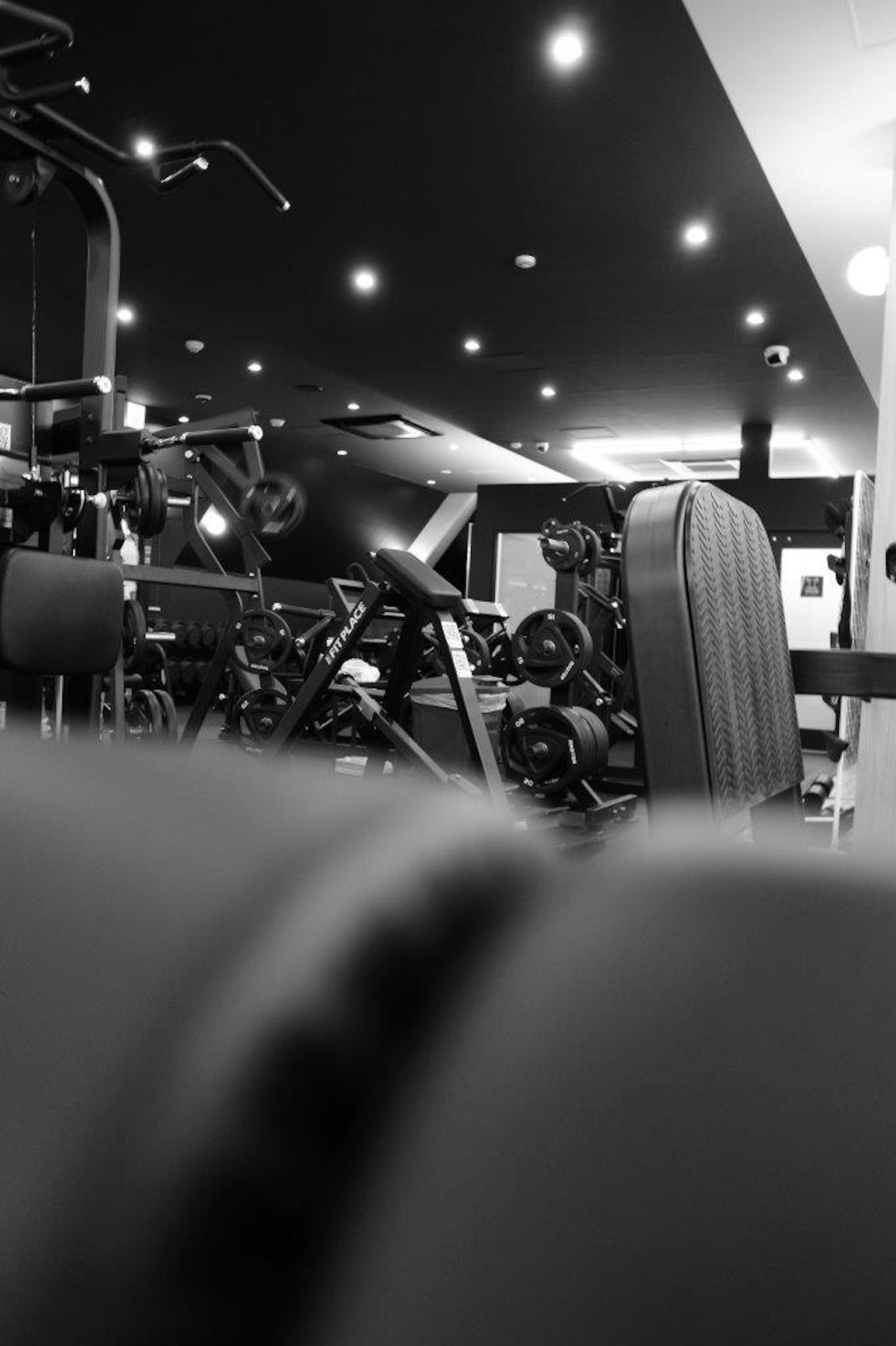 Immagine in bianco e nero dell'interno di una palestra con vari attrezzi e pesi