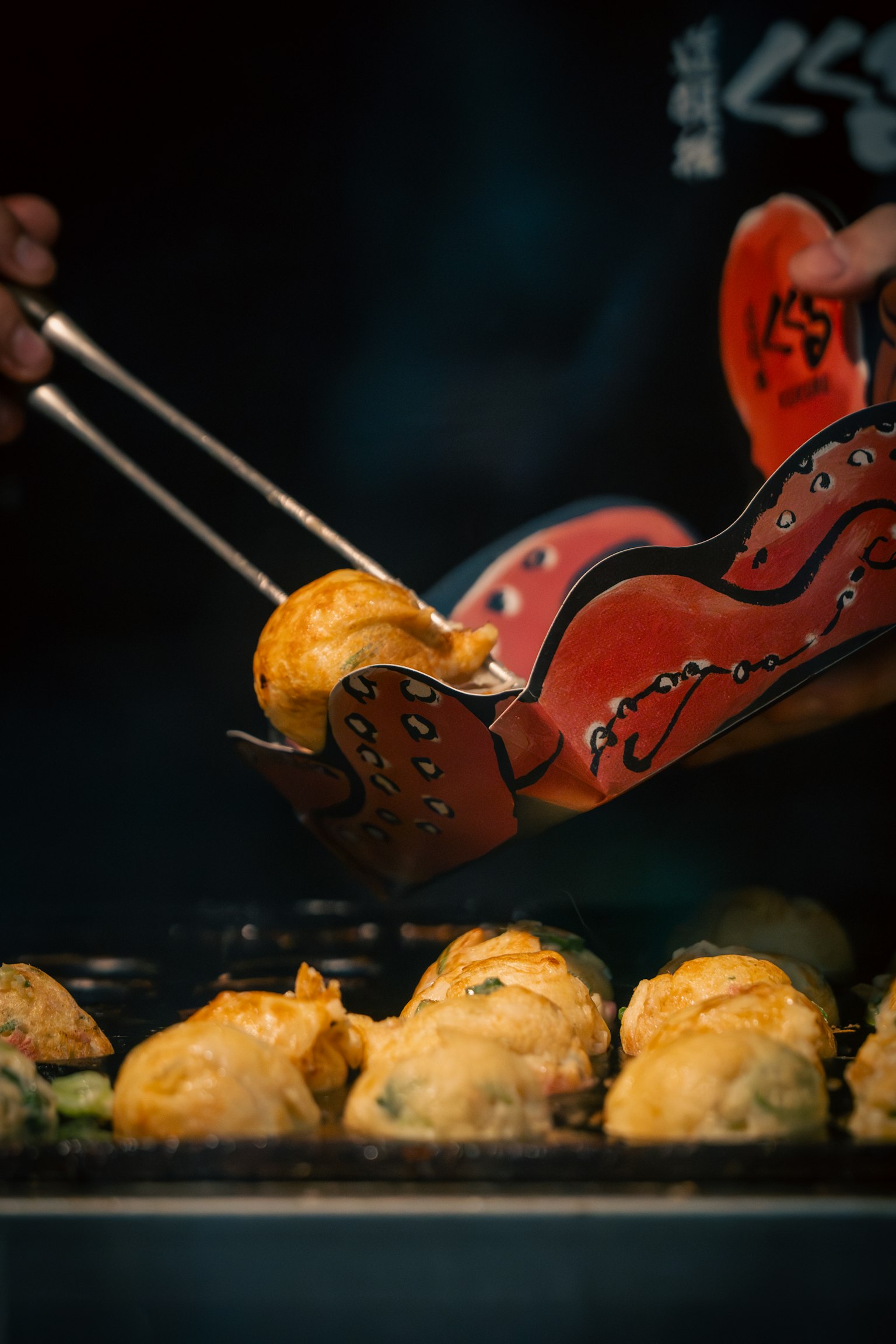 Hand holding red tongs picking up freshly cooked takoyaki