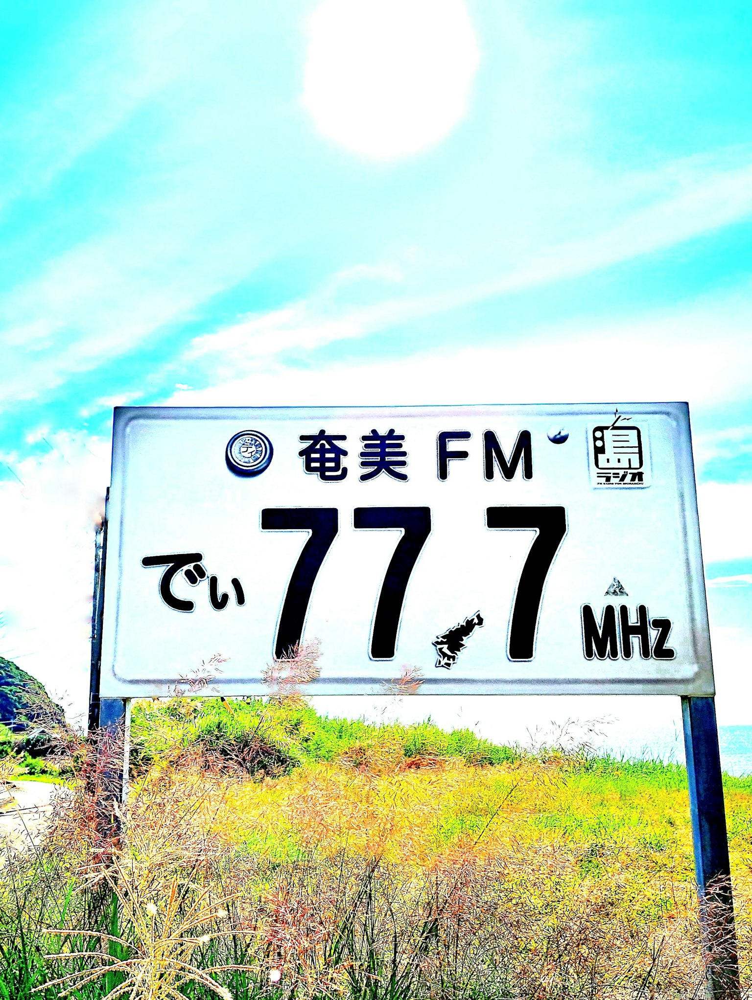 Cartel de una estación de radio FM en 77.7 MHz bajo un cielo azul