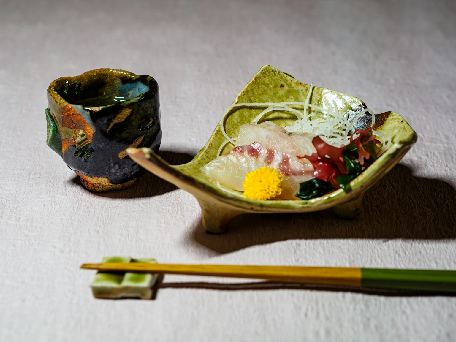 Sashimi servi sur une assiette élégante avec des baguettes vertes et une tasse à saké en céramique