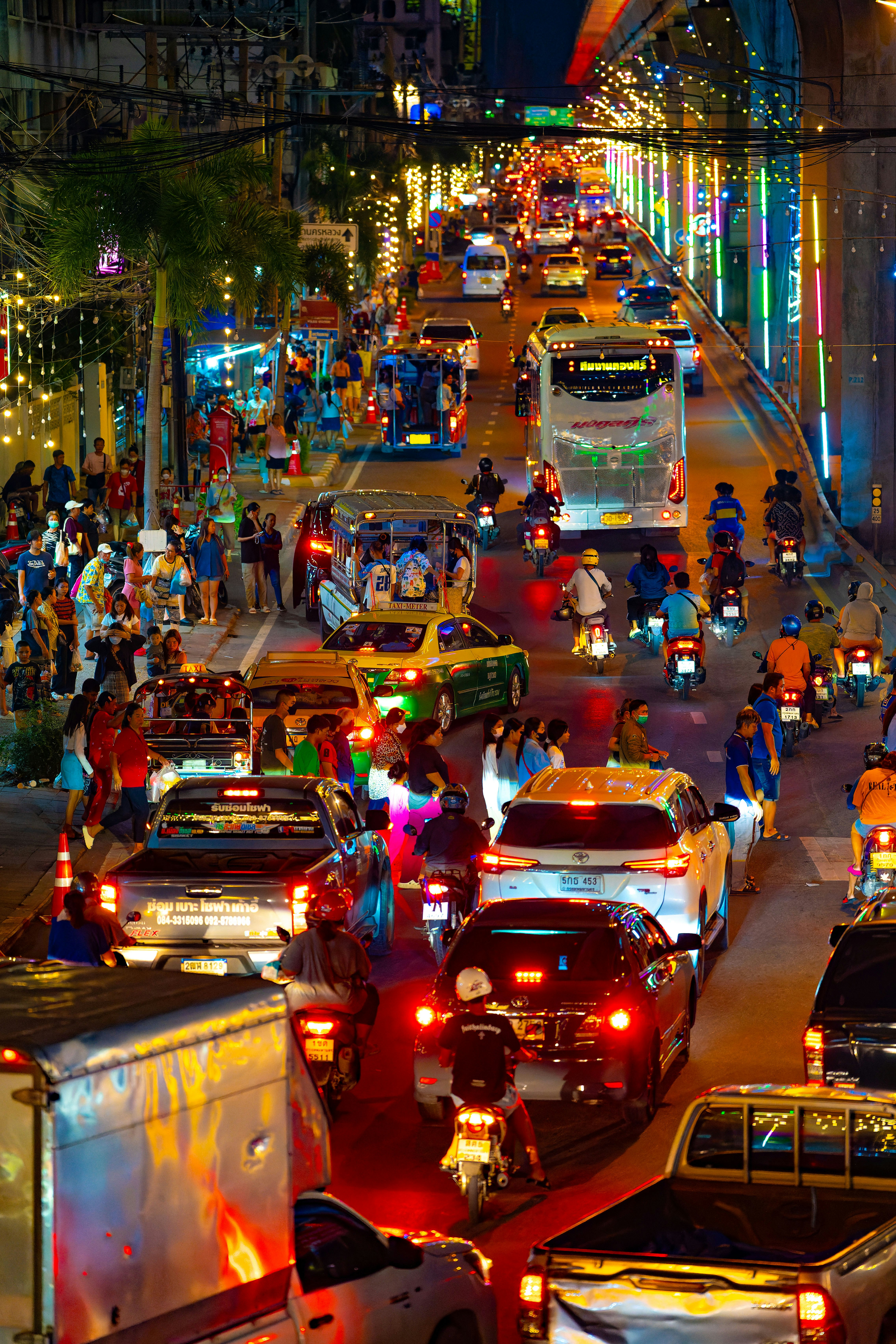 Una calle de fiesta abarrotada de coches y personas bajo luces coloridas