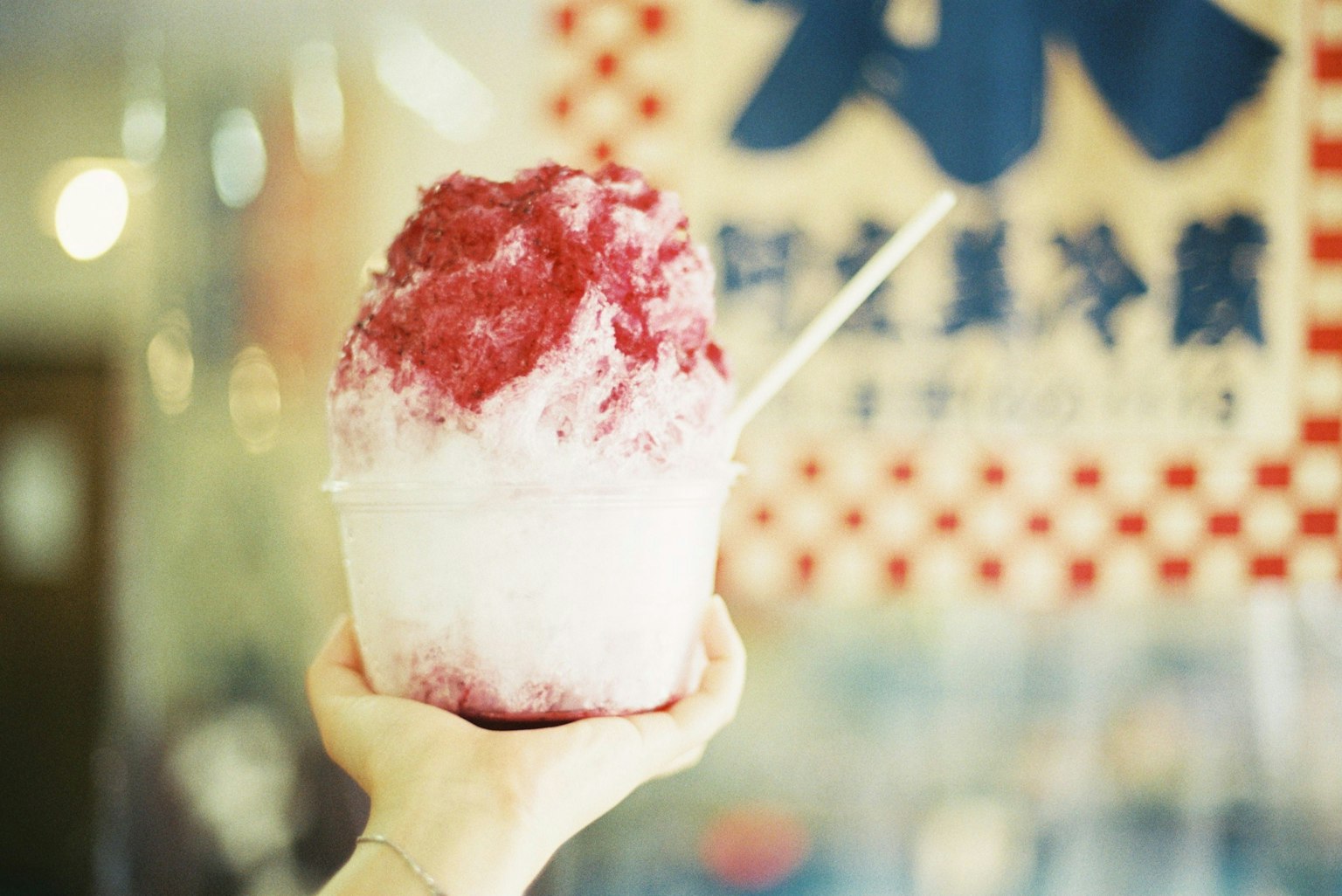 A hand holding a bowl of shaved ice topped with red syrup