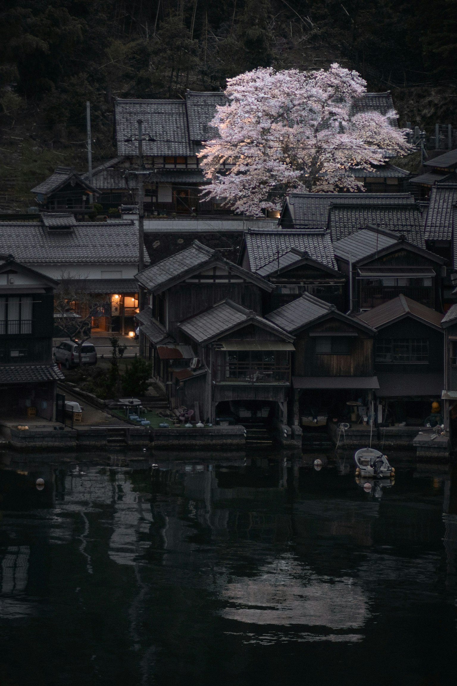 Una escena nocturna tranquila con un cerezo y casas tradicionales junto al agua