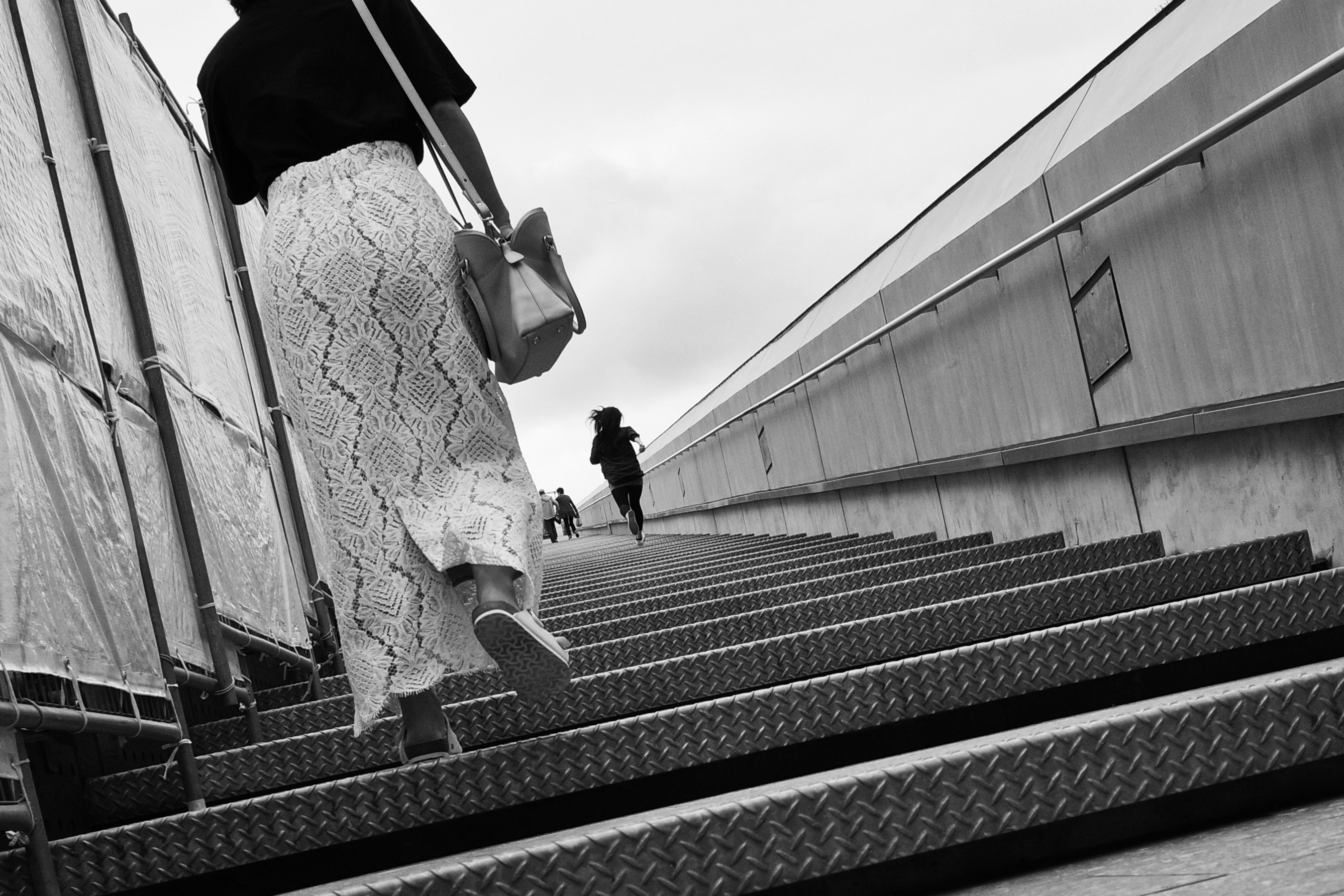Image en noir et blanc d'une femme montant des escaliers une autre silhouette en arrière-plan