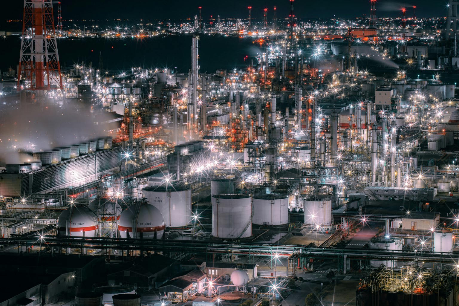夜の工業地帯の明るい風景 大きなタンクと煙突が見える