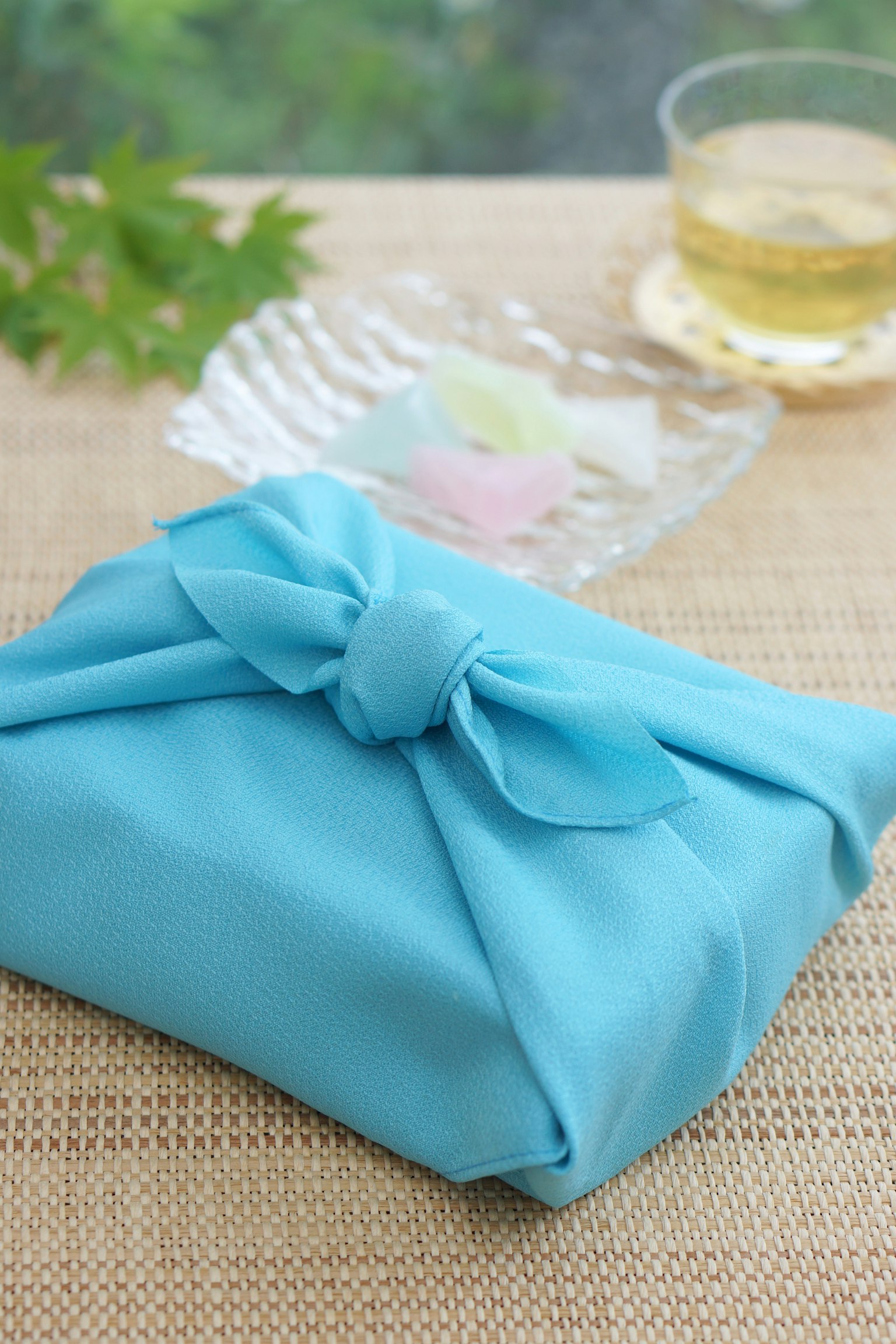 Un regalo avvolto in un tessuto blu con foglie verdi e un bicchiere di tè