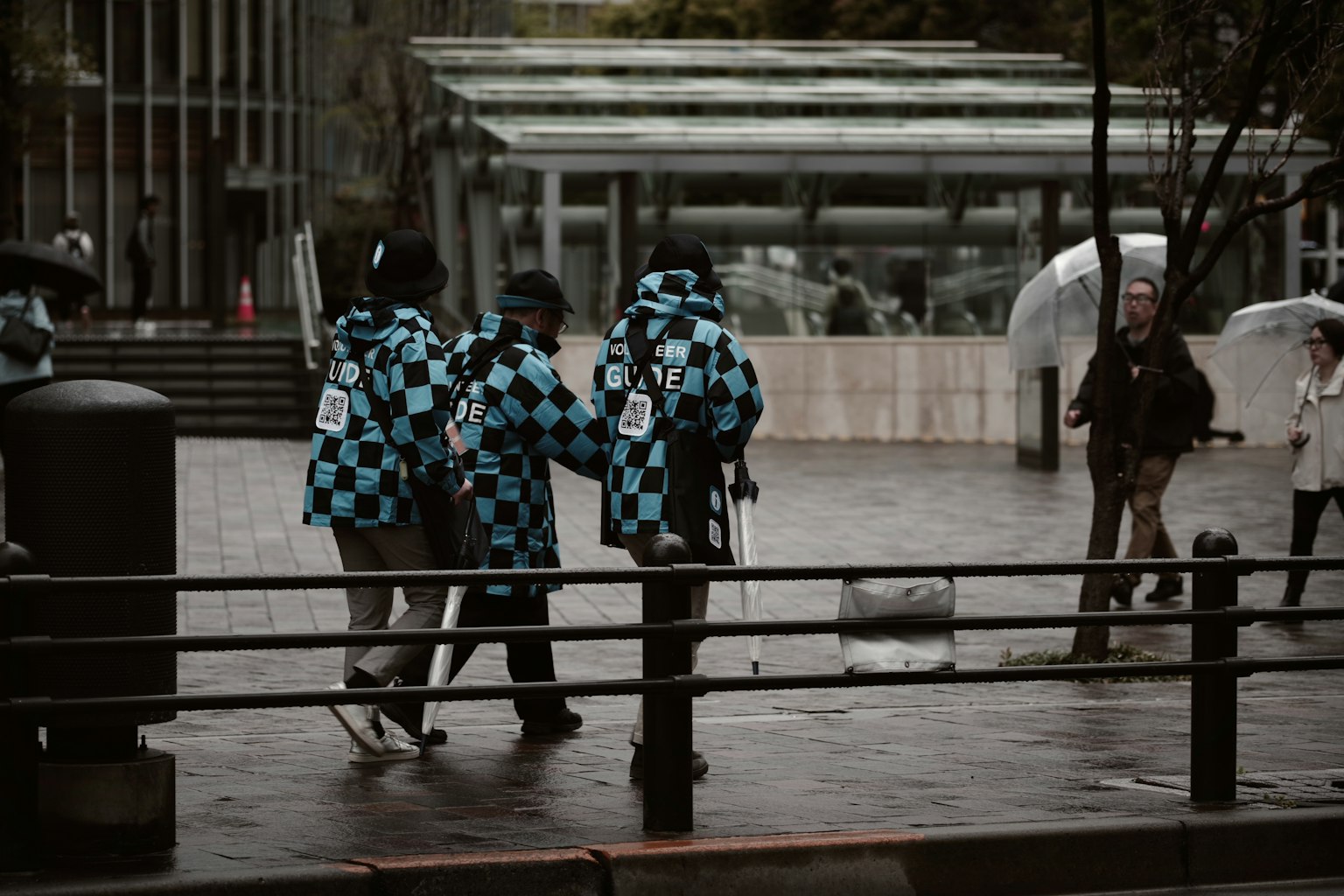 Personas con chaquetas a cuadros azules y negros caminando en un entorno urbano lluvioso