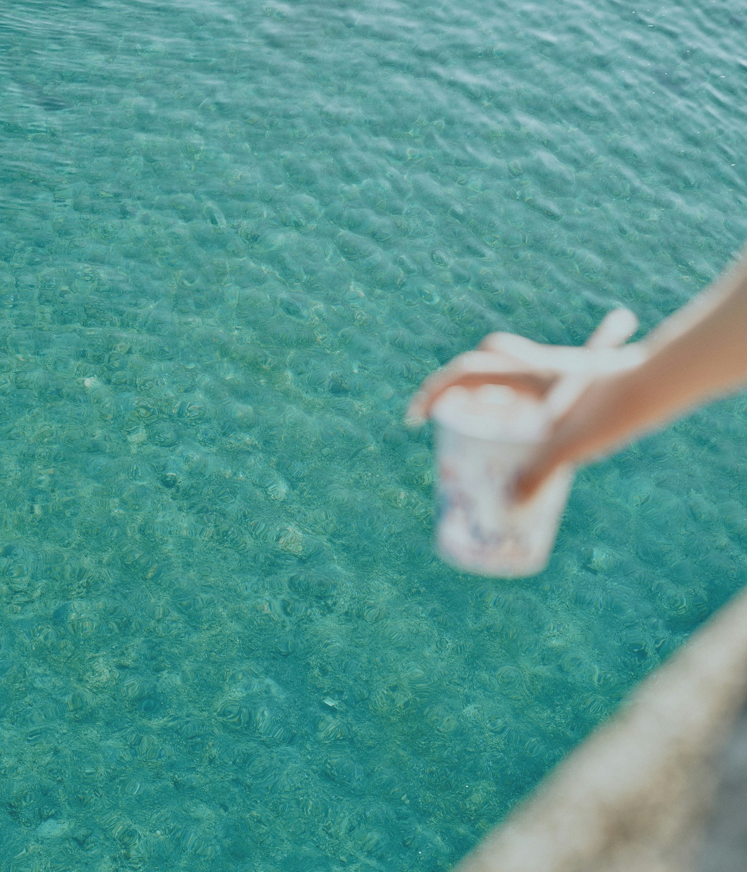 A hand holding a cup over a clear water surface