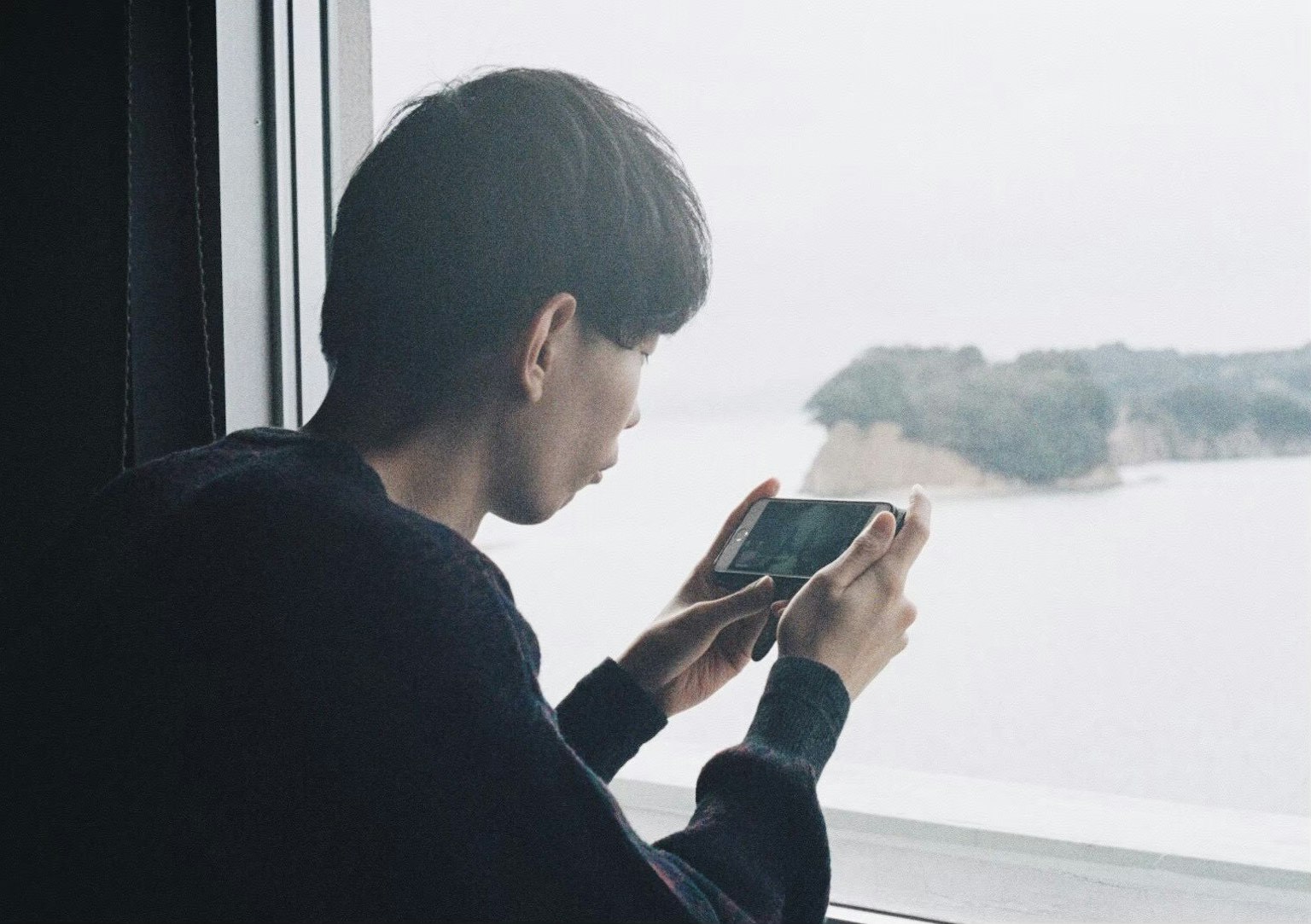 Junger Mensch macht ein Foto mit dem Smartphone, während er aus dem Fenster schaut