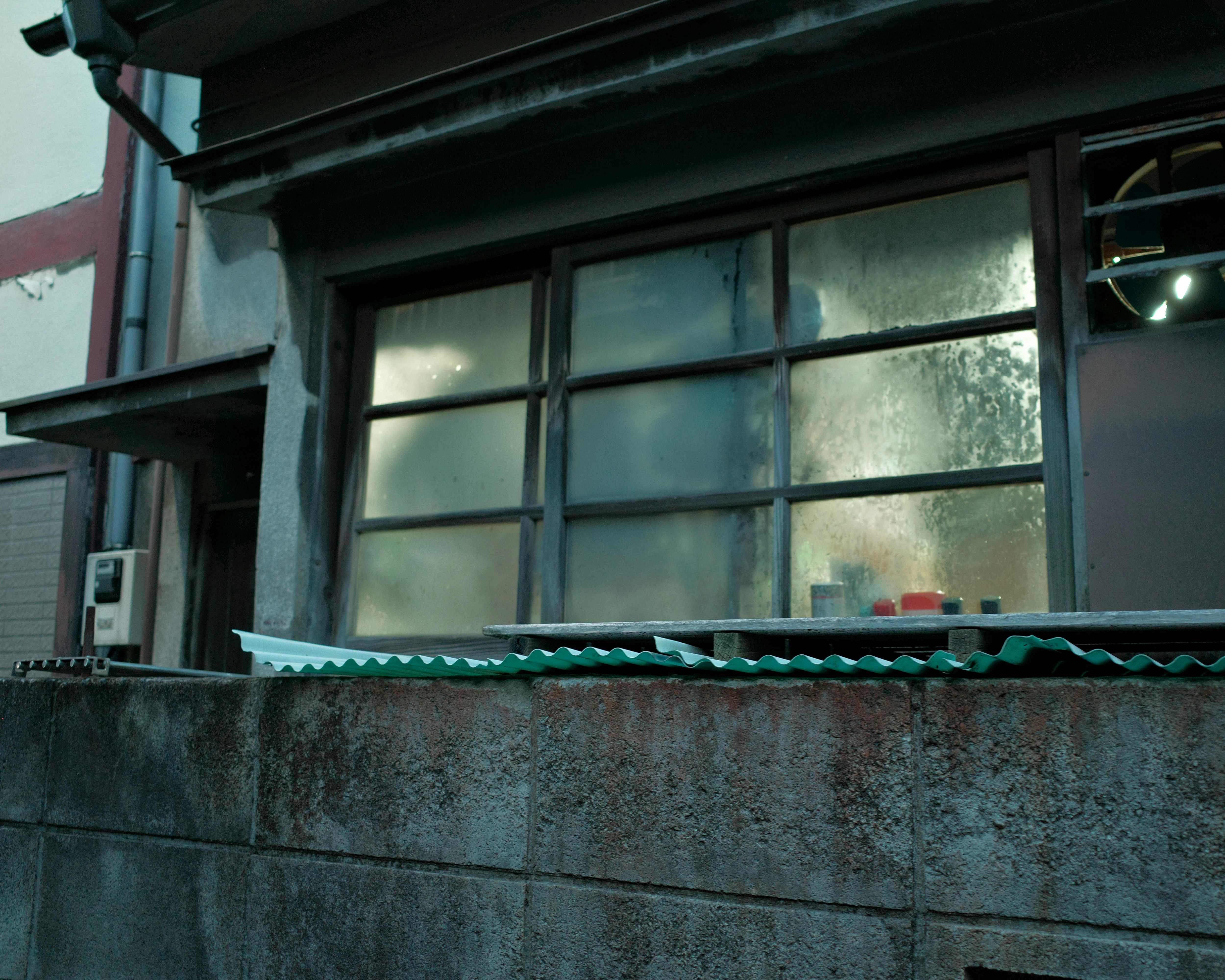 コンクリート塀の上に並ぶ波形の屋根材と窓のある外壁