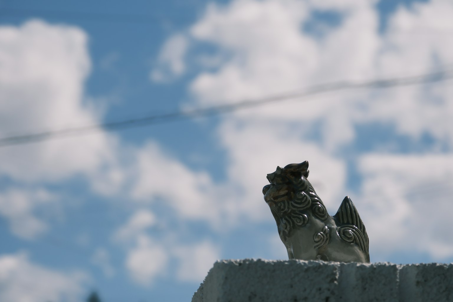 Statua di pollo in pietra contro un cielo blu con nuvole