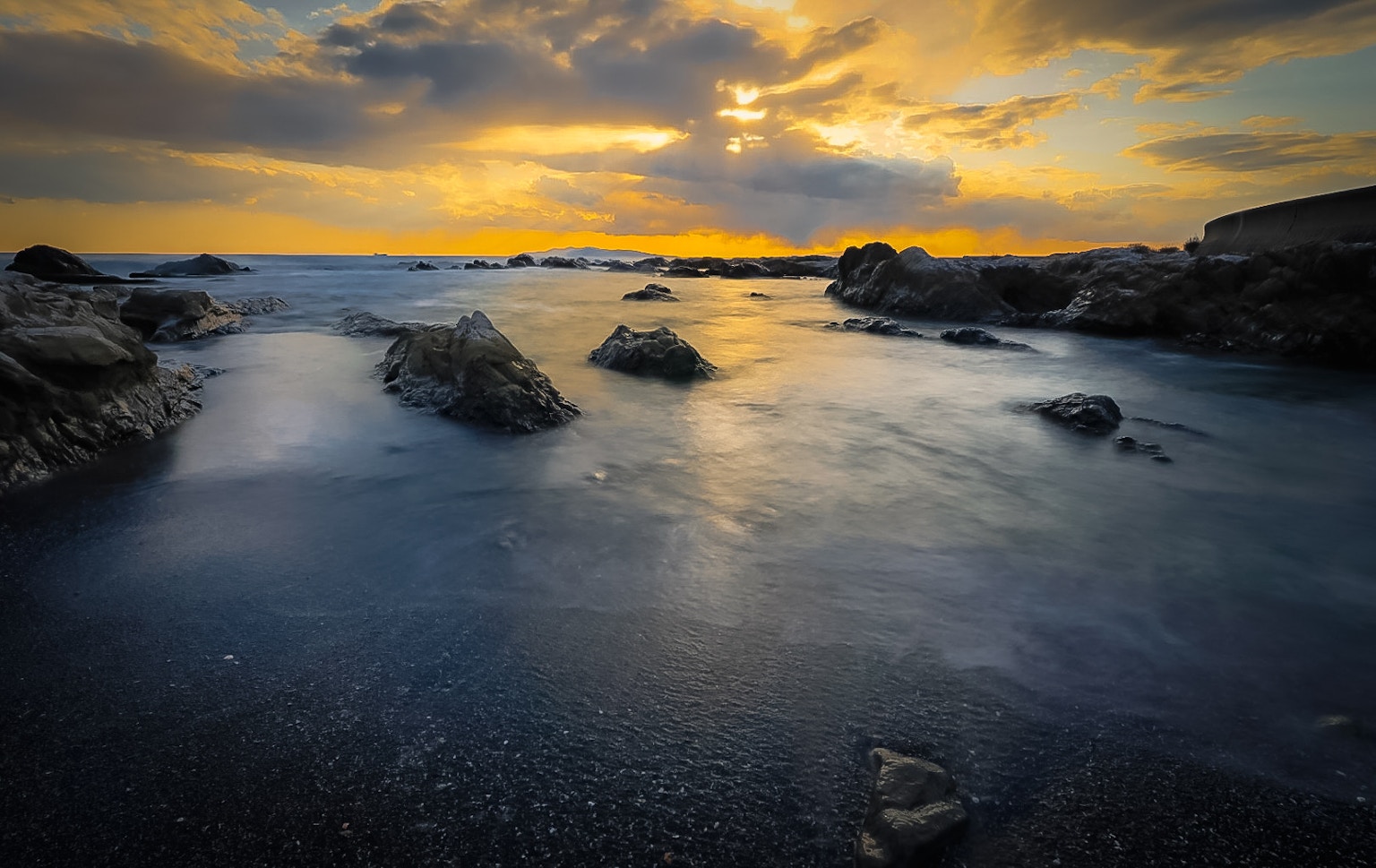 Pemandangan pantai saat matahari terbenam dengan batu dan ombak lembut