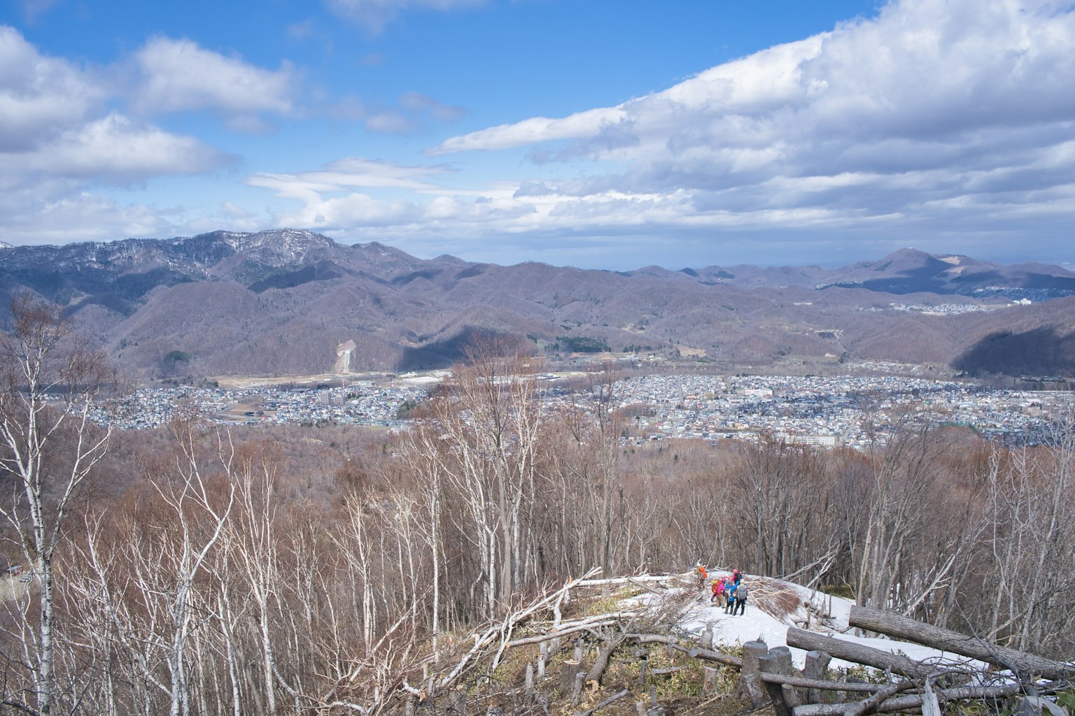 ทิวทัศน์พาโนรามาจากยอดเขาแสดงภูมิทัศน์ฤดูหนาวและเมืองด้านล่างใต้ท้องฟ้าสีฟ้ากับเมฆสีขาว