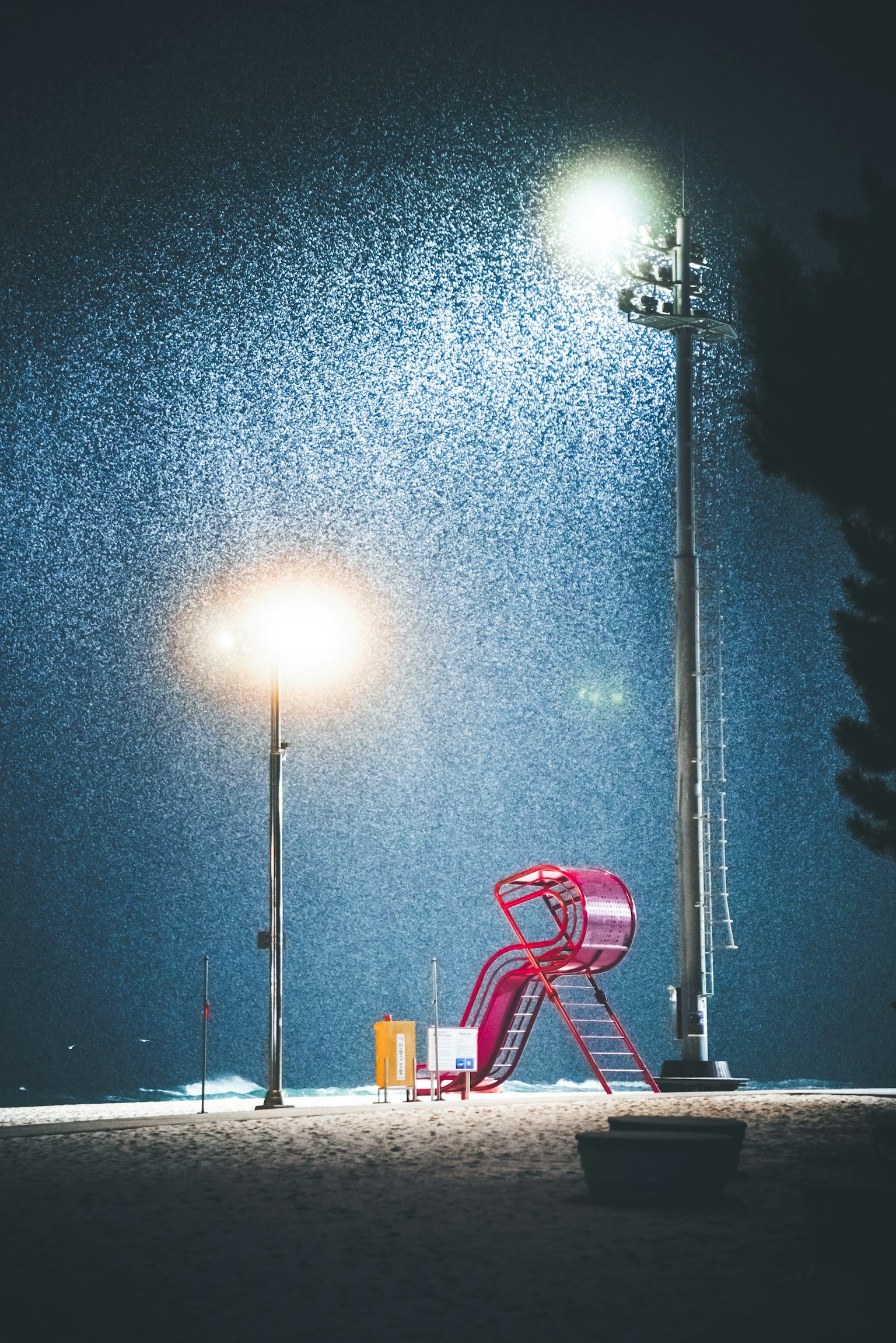 夜の公園にある赤い滑り台と街灯の下で降る雪