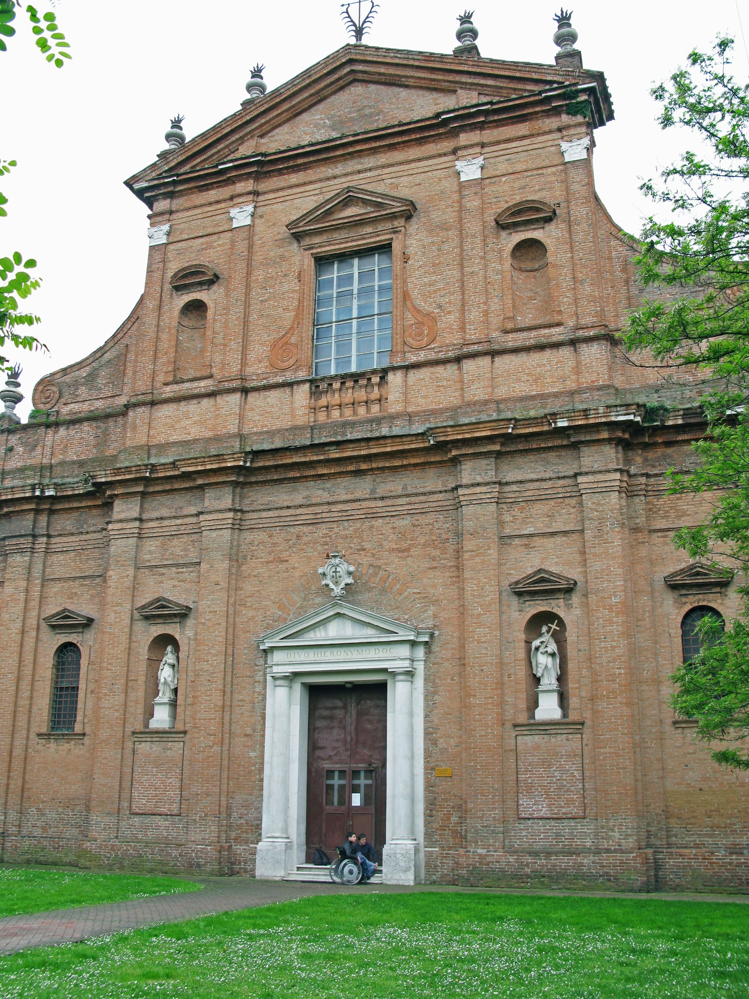 Fachada de una iglesia marrón rojizo con ventanas y esculturas puerta de madera rodeada de césped verde
