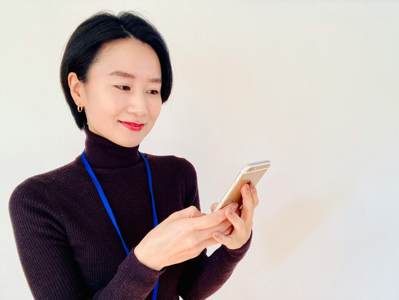 一位女性正在使用智能手机，穿着黑色高领毛衣和蓝色挂绳