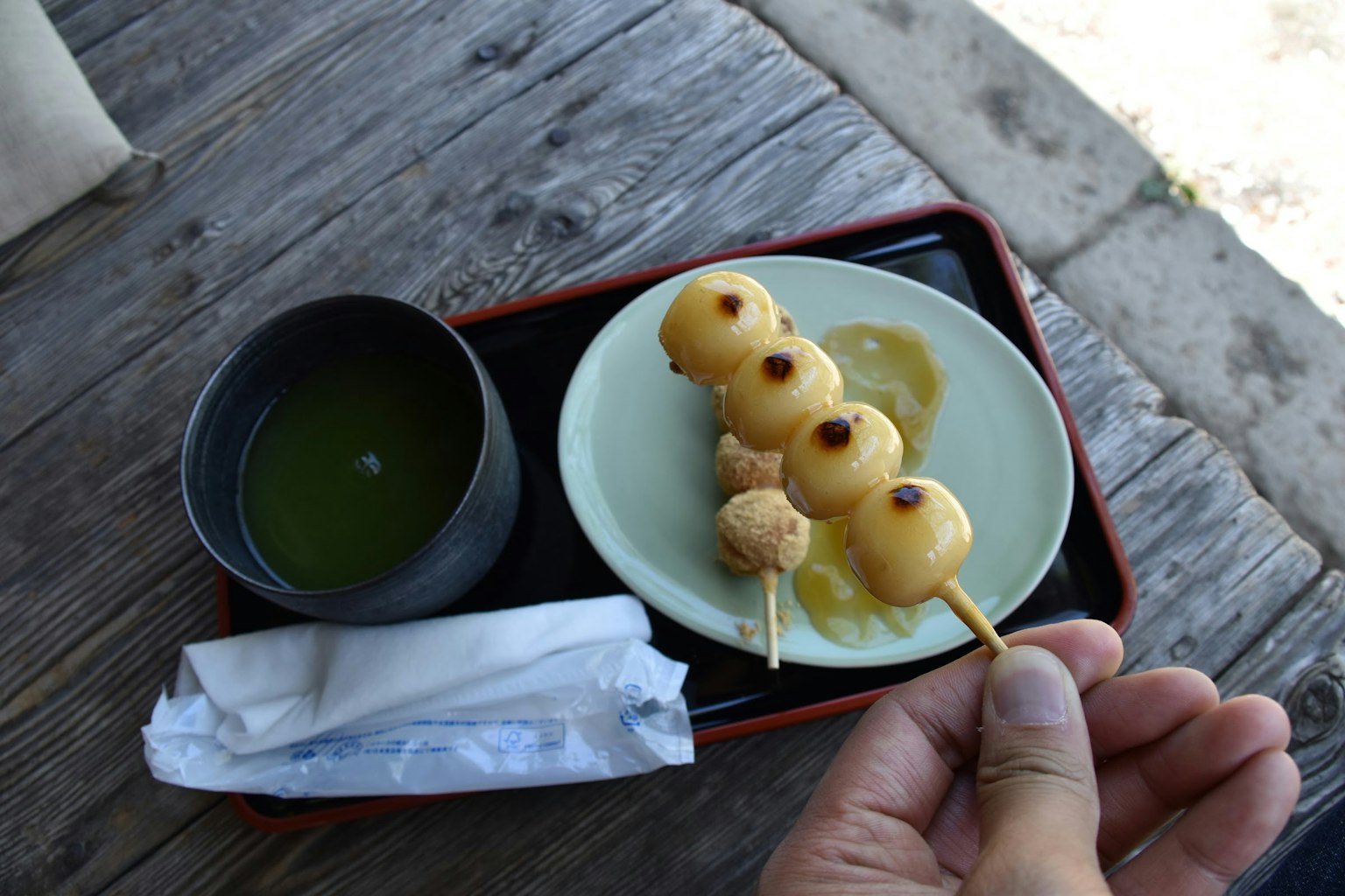 Brochettes de dango tenues dans une main avec une tasse de thé vert