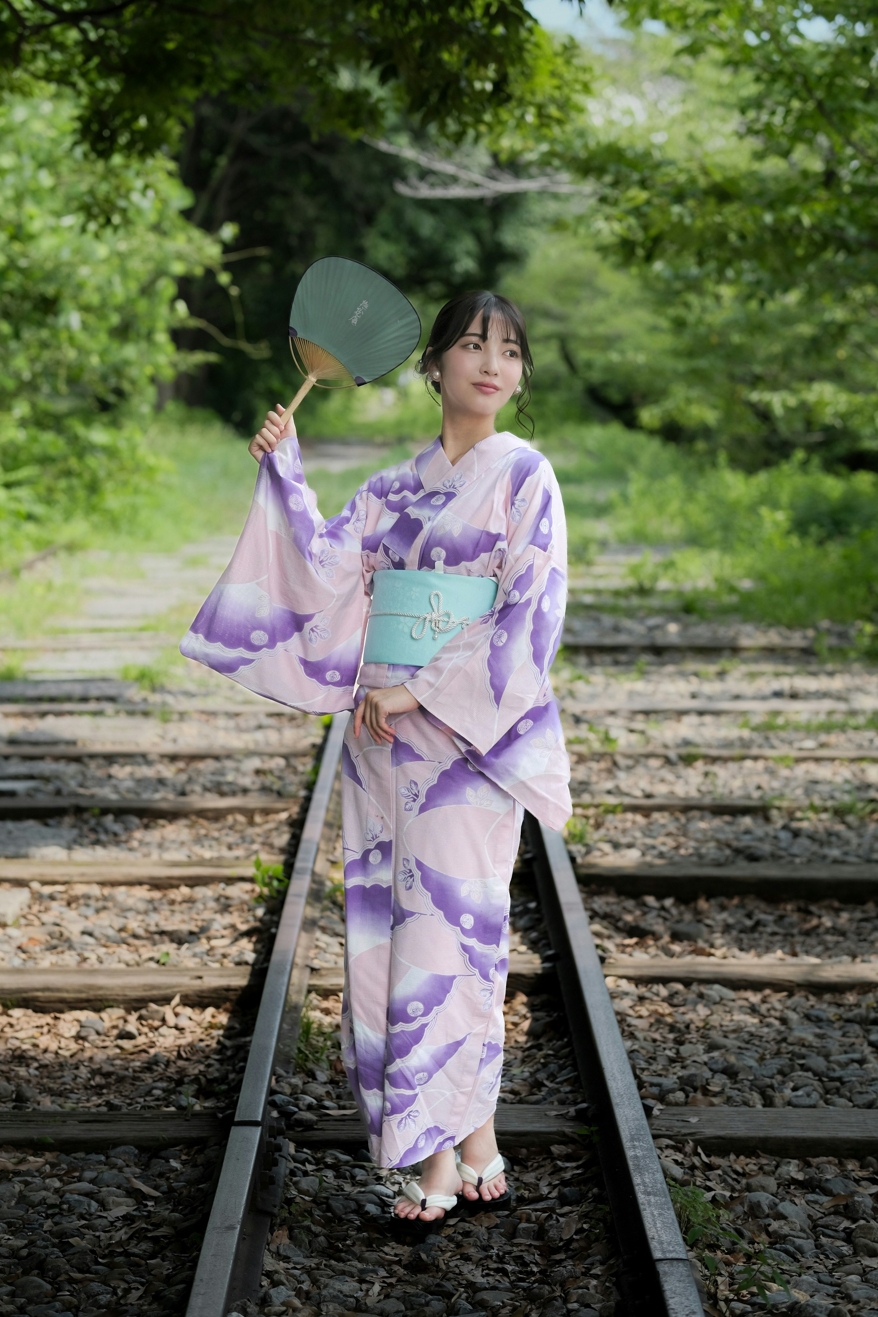 線路上でうちわを持つ浴衣姿のモデル