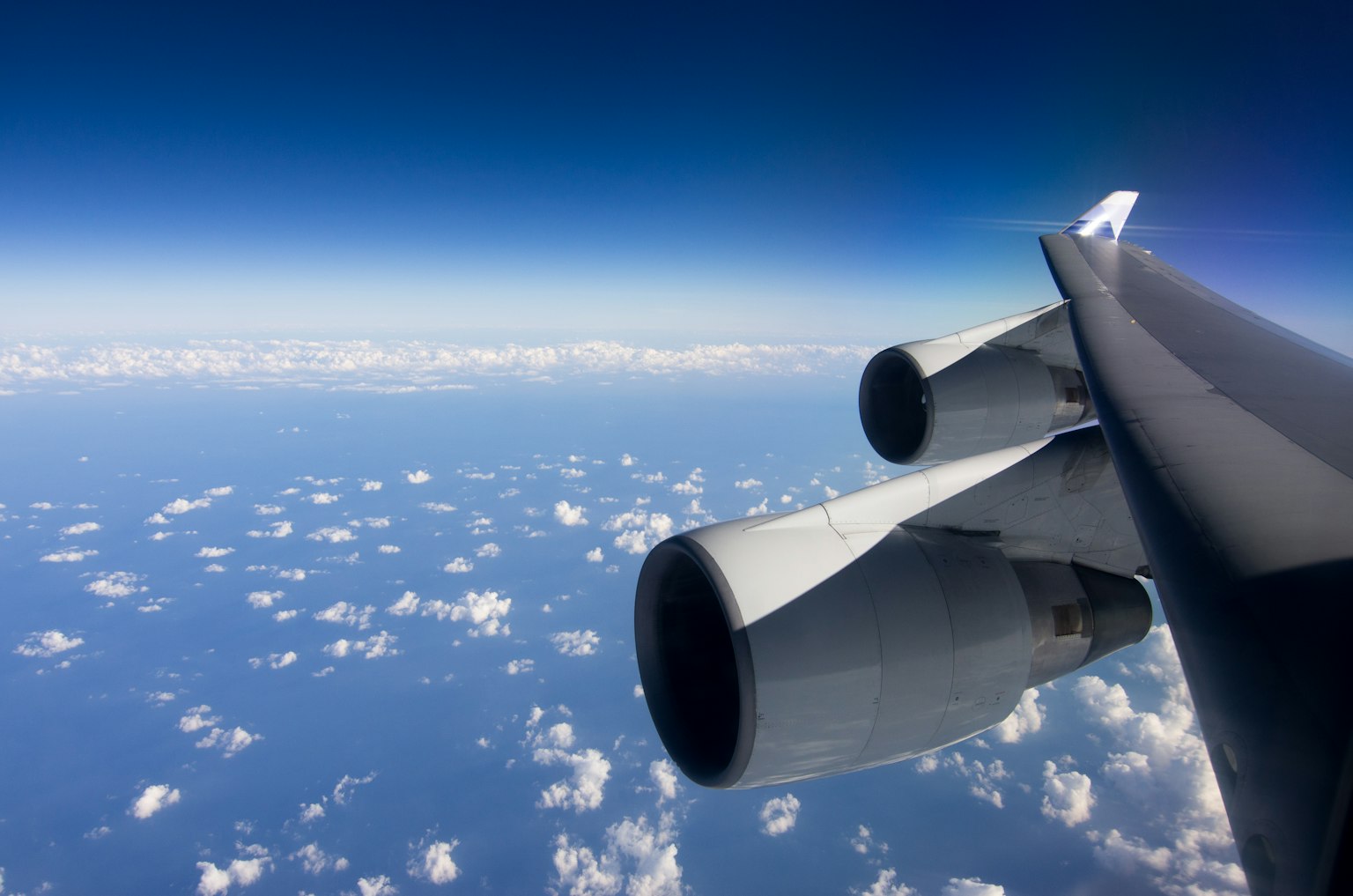 View of an airplane wing and engine against a blue sky and clouds