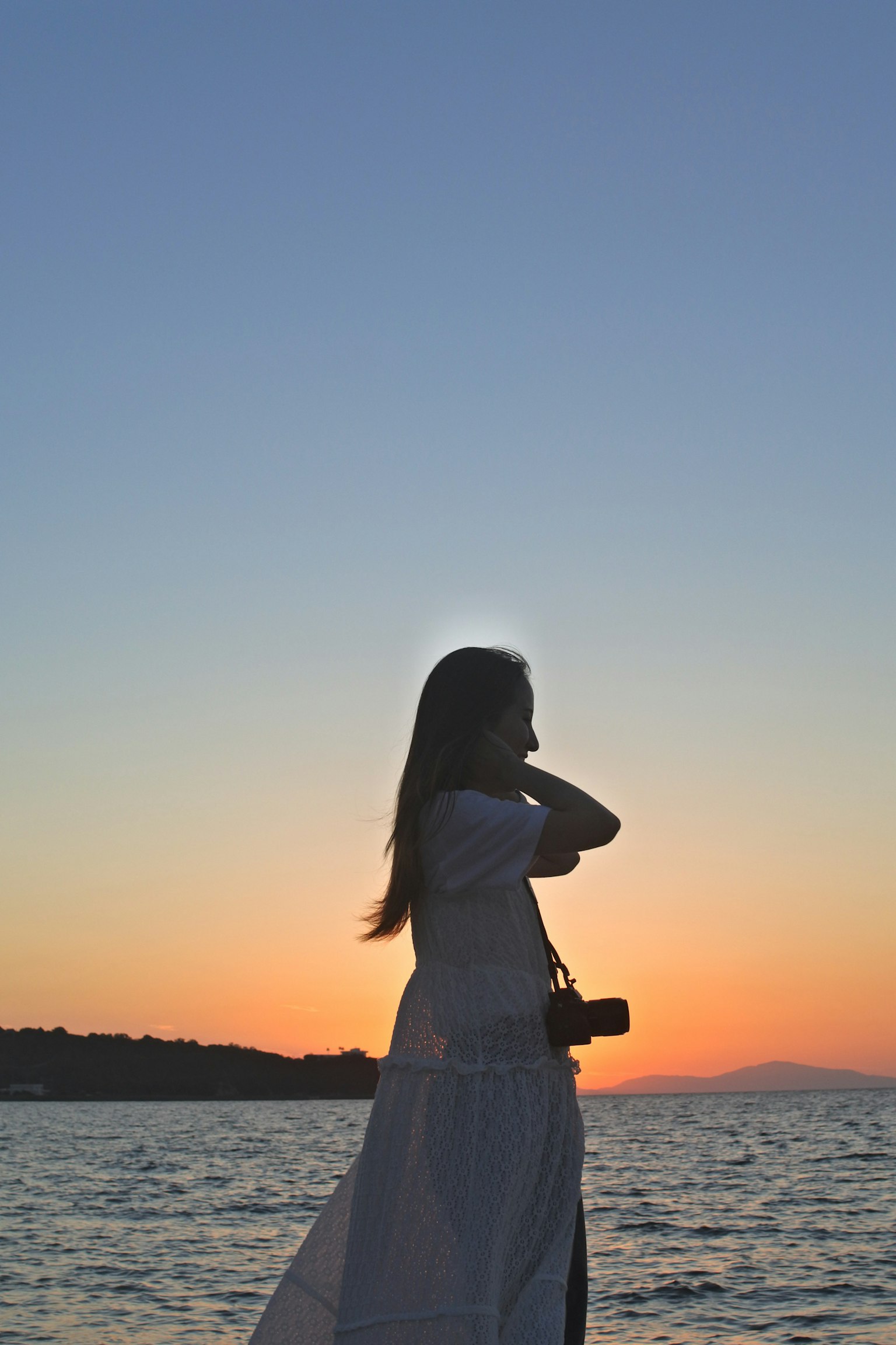夕日を背景にした女性のシルエットが海の近くに立っている