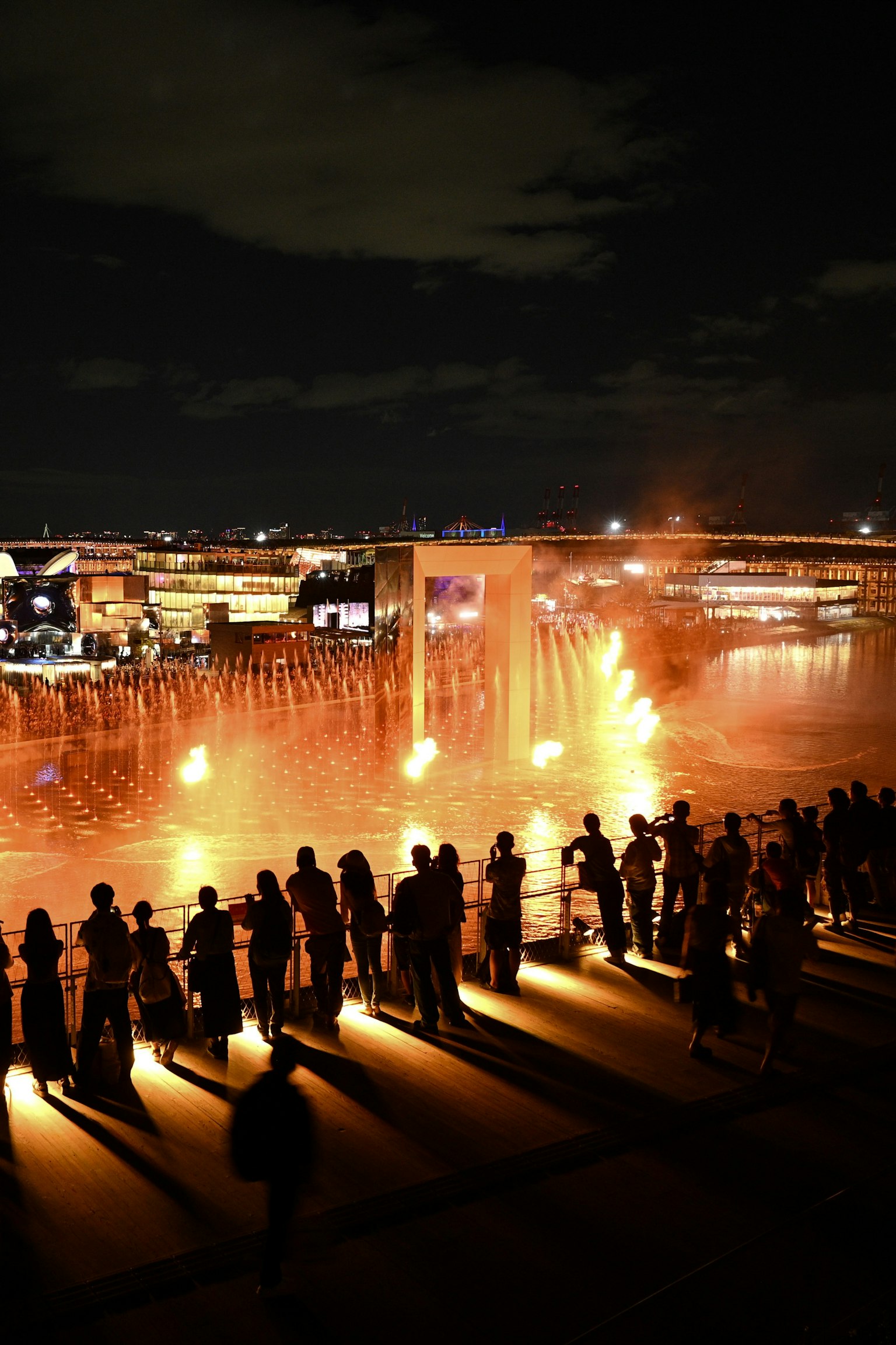 Siluet penonton menikmati pertunjukan air mancur malam dengan jet air berwarna-warni