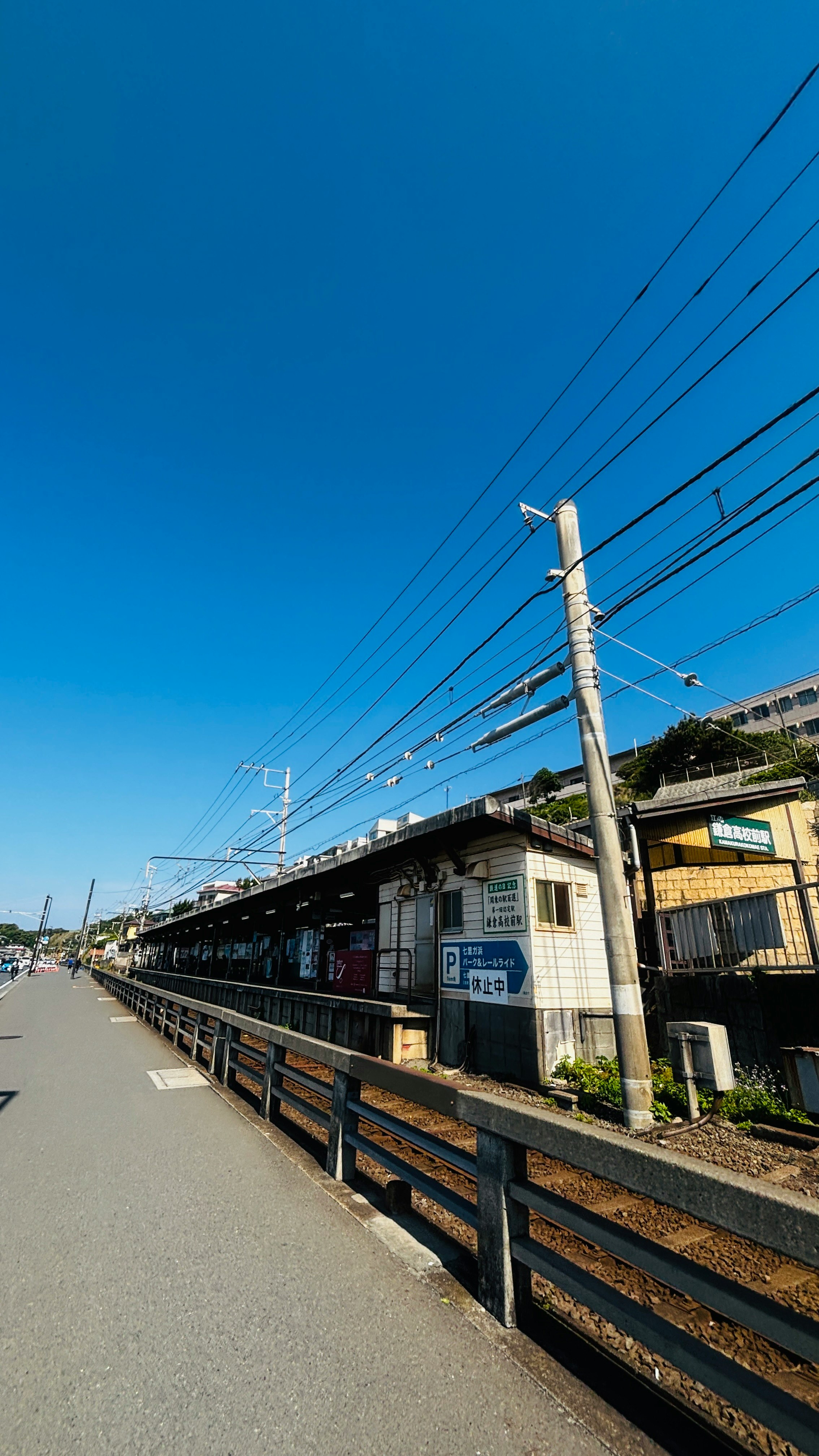 青空の下、線路沿いのフェンスと電柱が続く海辺の道
