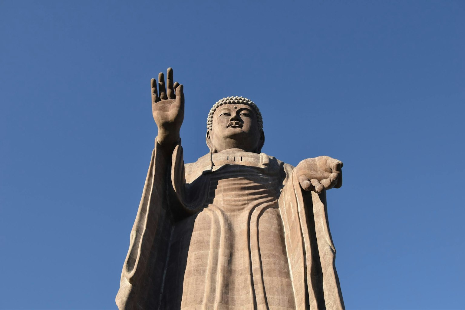 Grande statua di Buddha che alza la mano contro il cielo blu