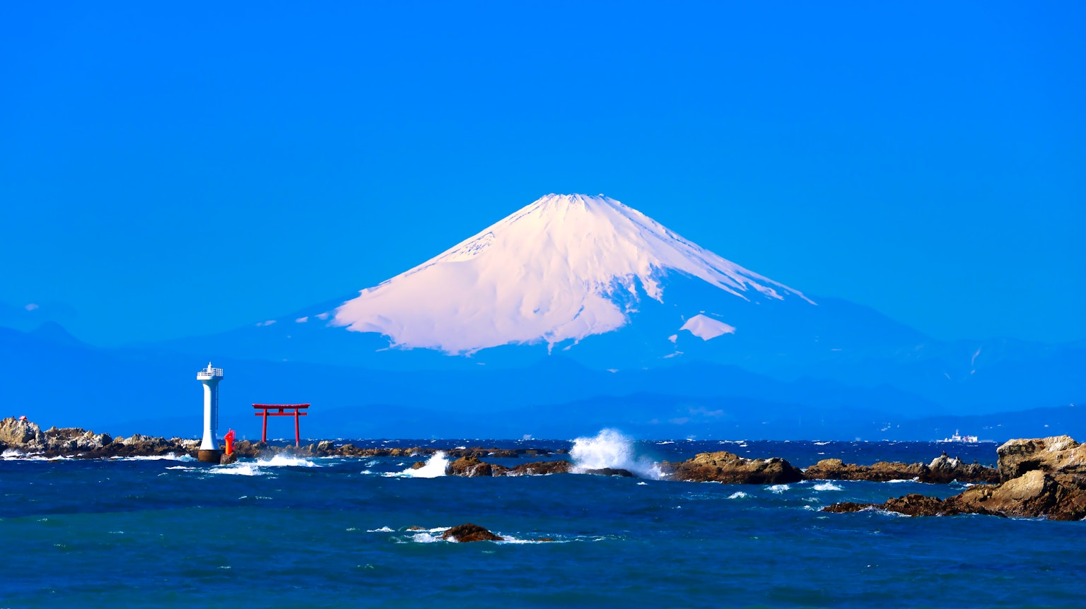 Le mont Fuji s'élève majestueusement contre un ciel bleu clair avec un torii rouge au premier plan