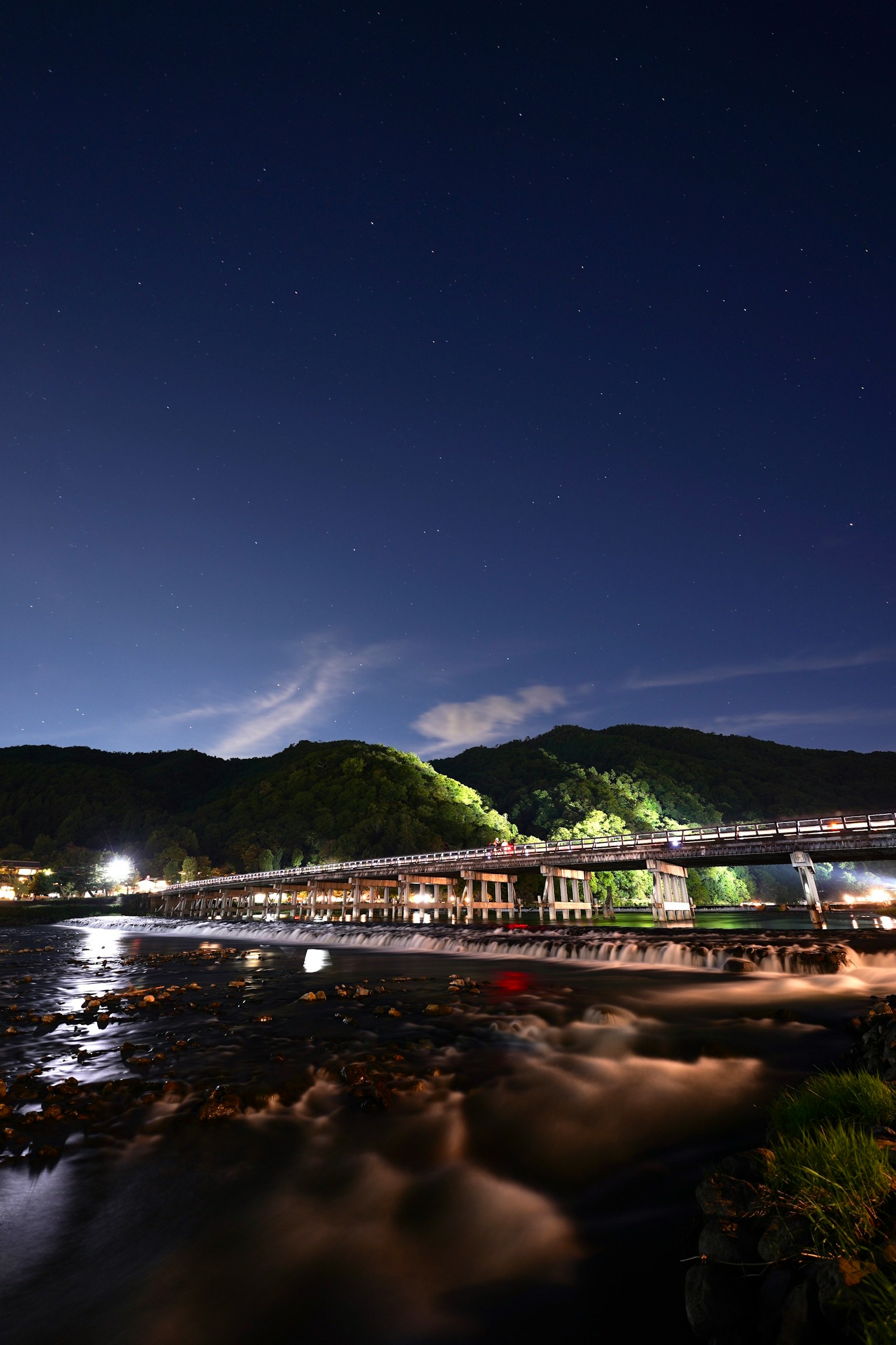별빛이 비치는 하늘과 녹색 언덕이 있는 강과 다리의 야경
