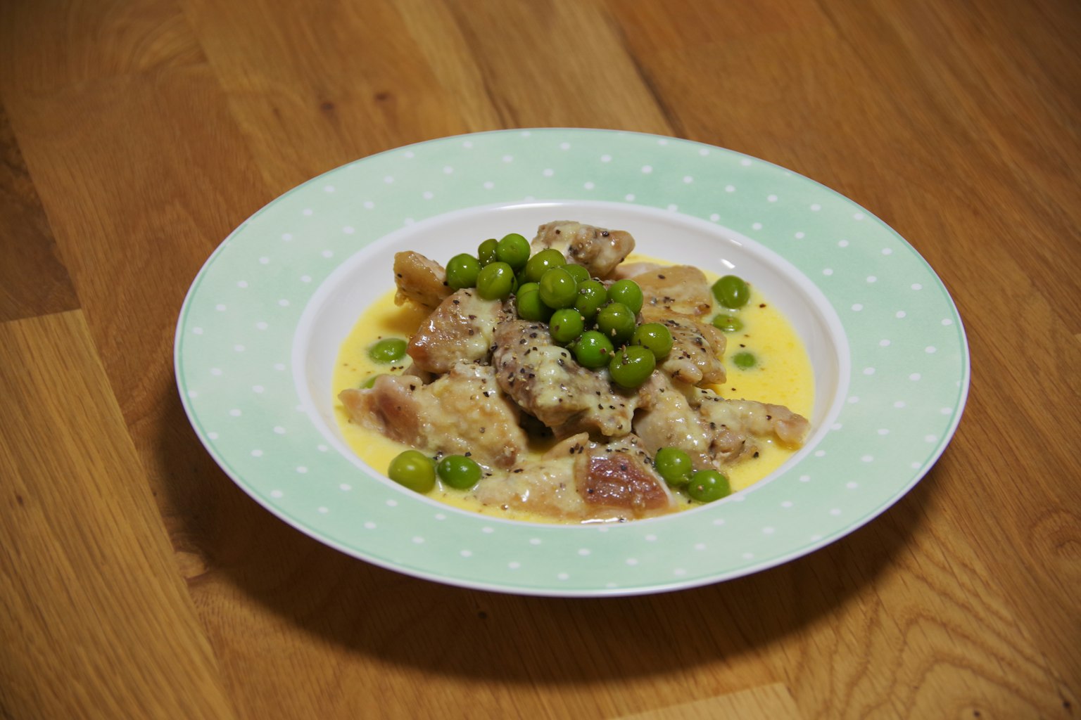 Piatto di carne cremoso guarnito con piselli verdi su un piatto decorativo