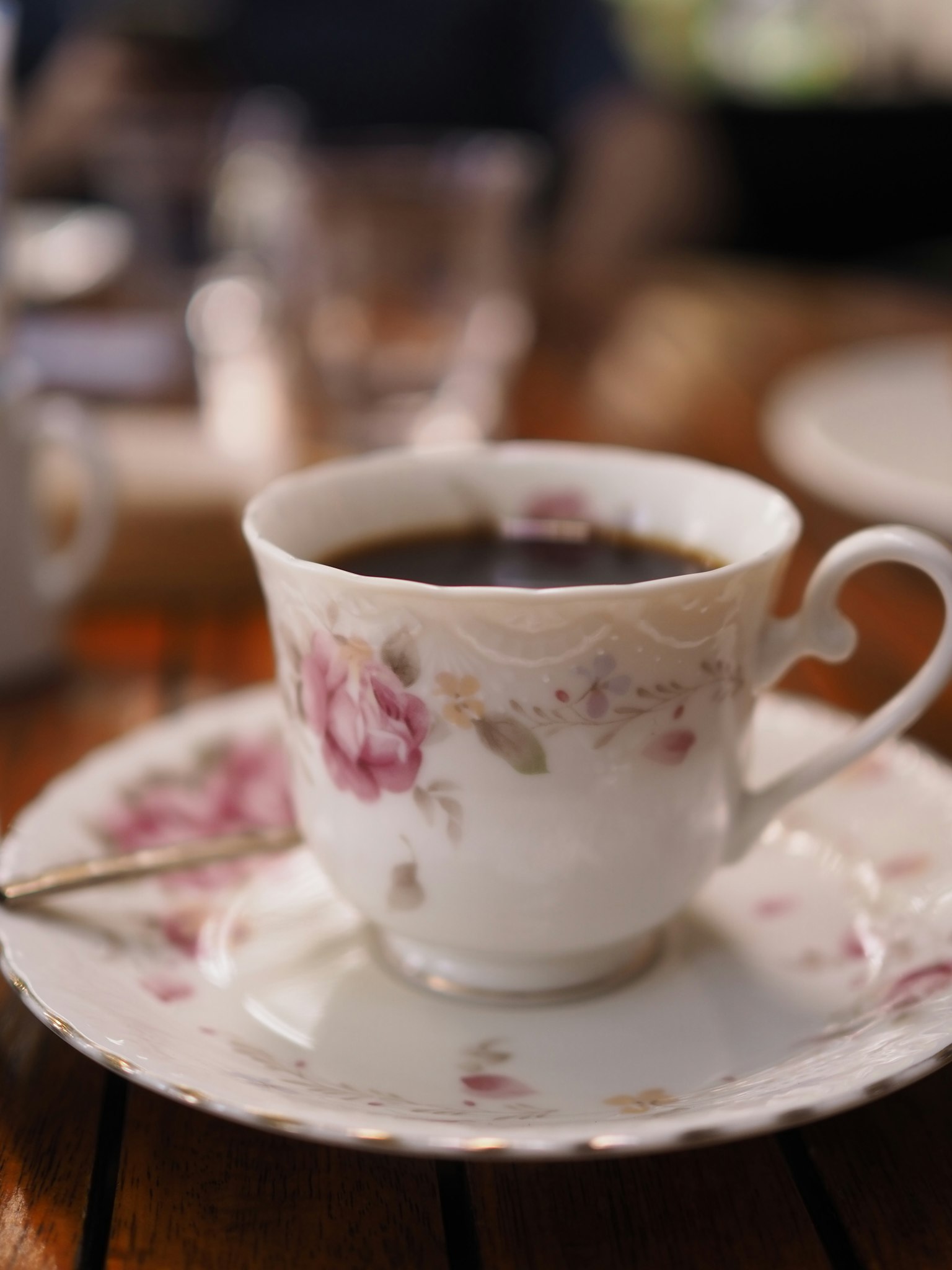 ถ้วยชาที่มีลวดลายดอกไม้สวยงามเต็มไปด้วยกาแฟดำบนโต๊ะ