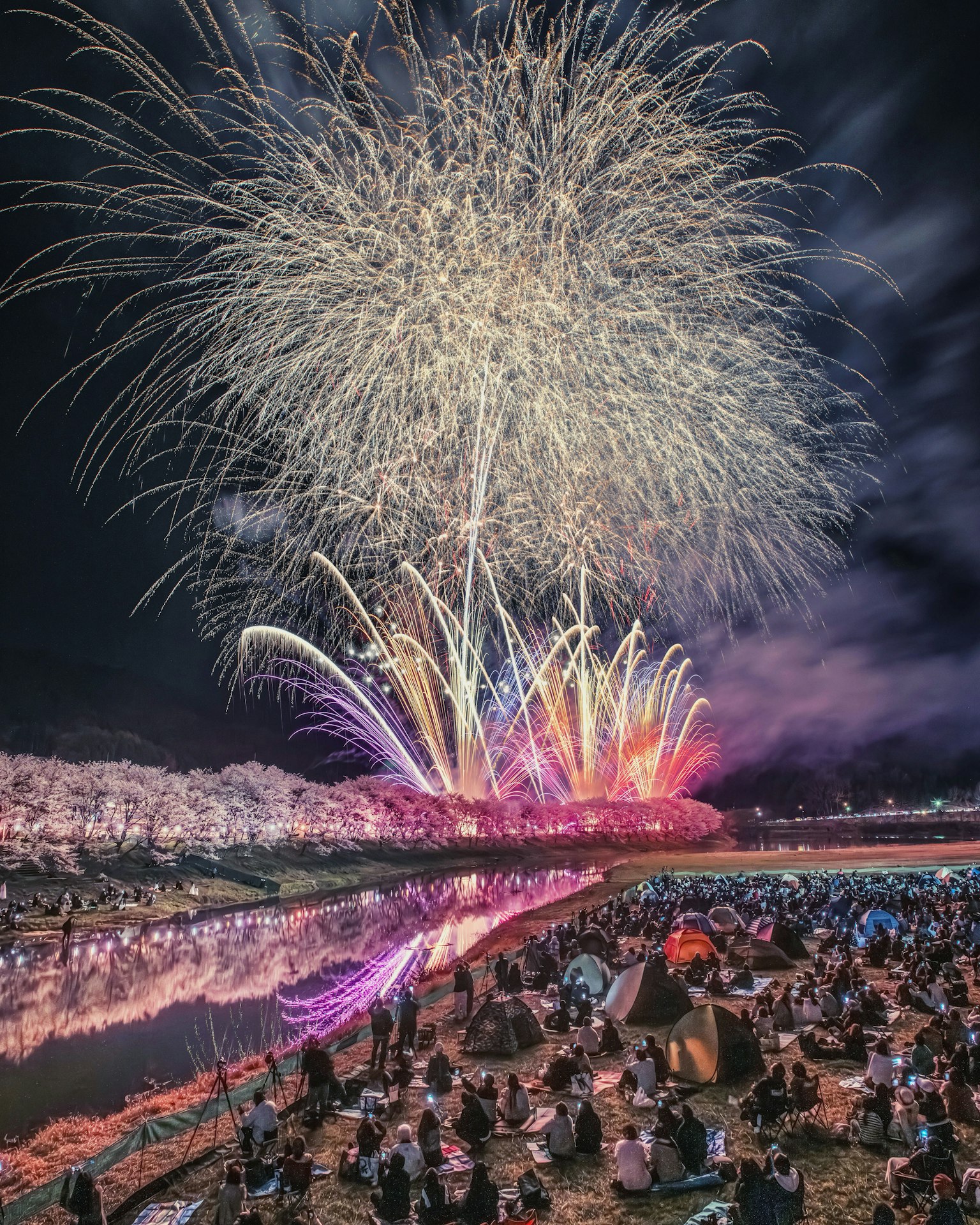 Spectaculaire feu d'artifice au-dessus d'une rivière avec une grande foule rassemblée sur la rive