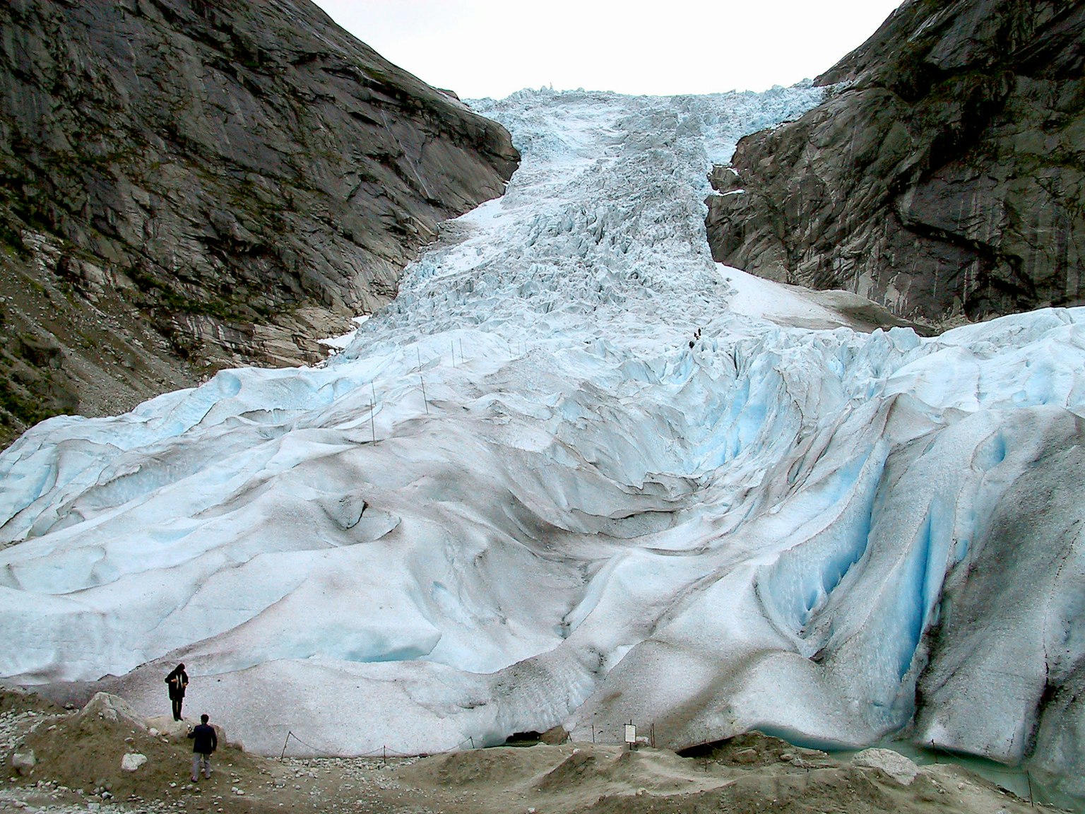 Une personne se tenant près d'un glacier coulant entre des falaises rocheuses