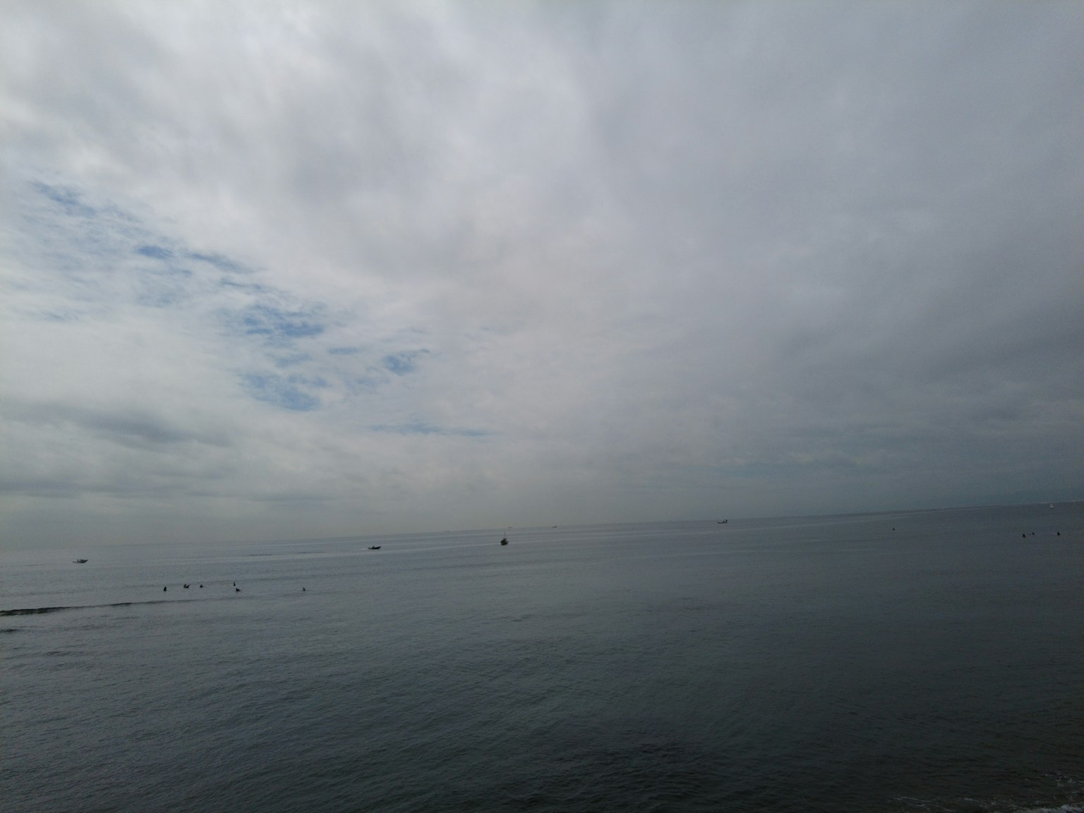 Ruhige Meereslandschaft unter einem bewölkten Himmel mit kleinen Booten in der Ferne