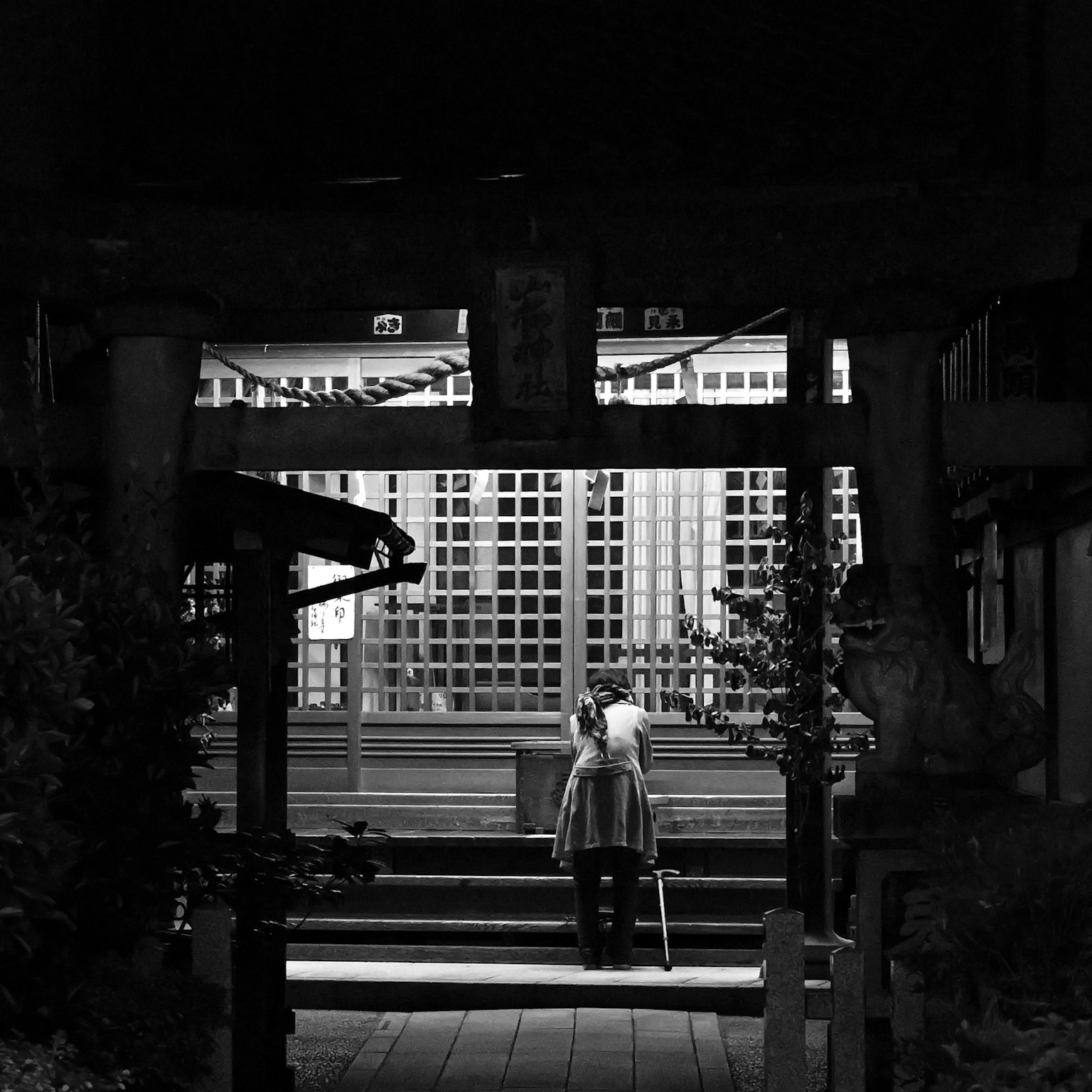 Silhouette of a woman standing in front of a shrine gate at night