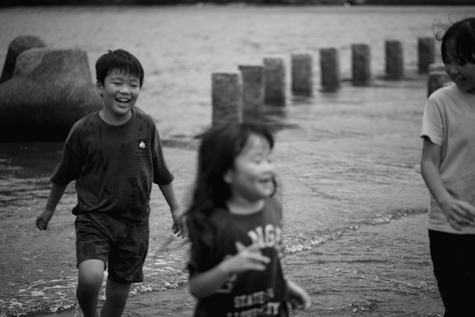 黑白照片，孩子们在水边玩耍，微笑奔跑，一个男孩和一个女孩，背景有石头防波堤