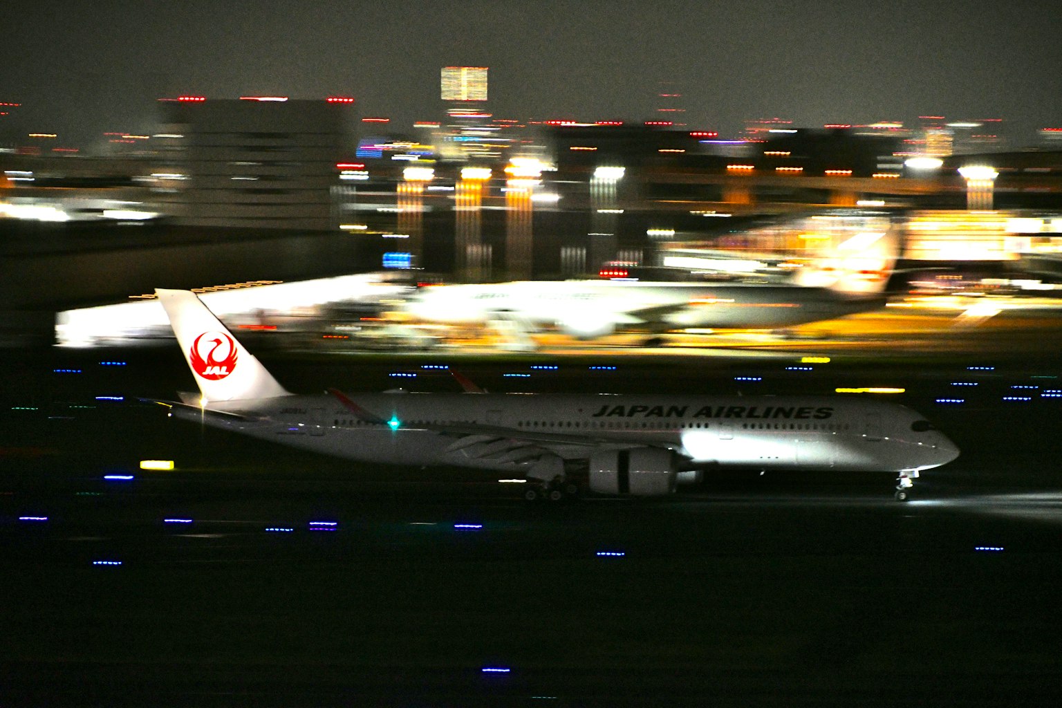 Avión de Japan Airlines despegando de noche con un fondo de ciudad borroso