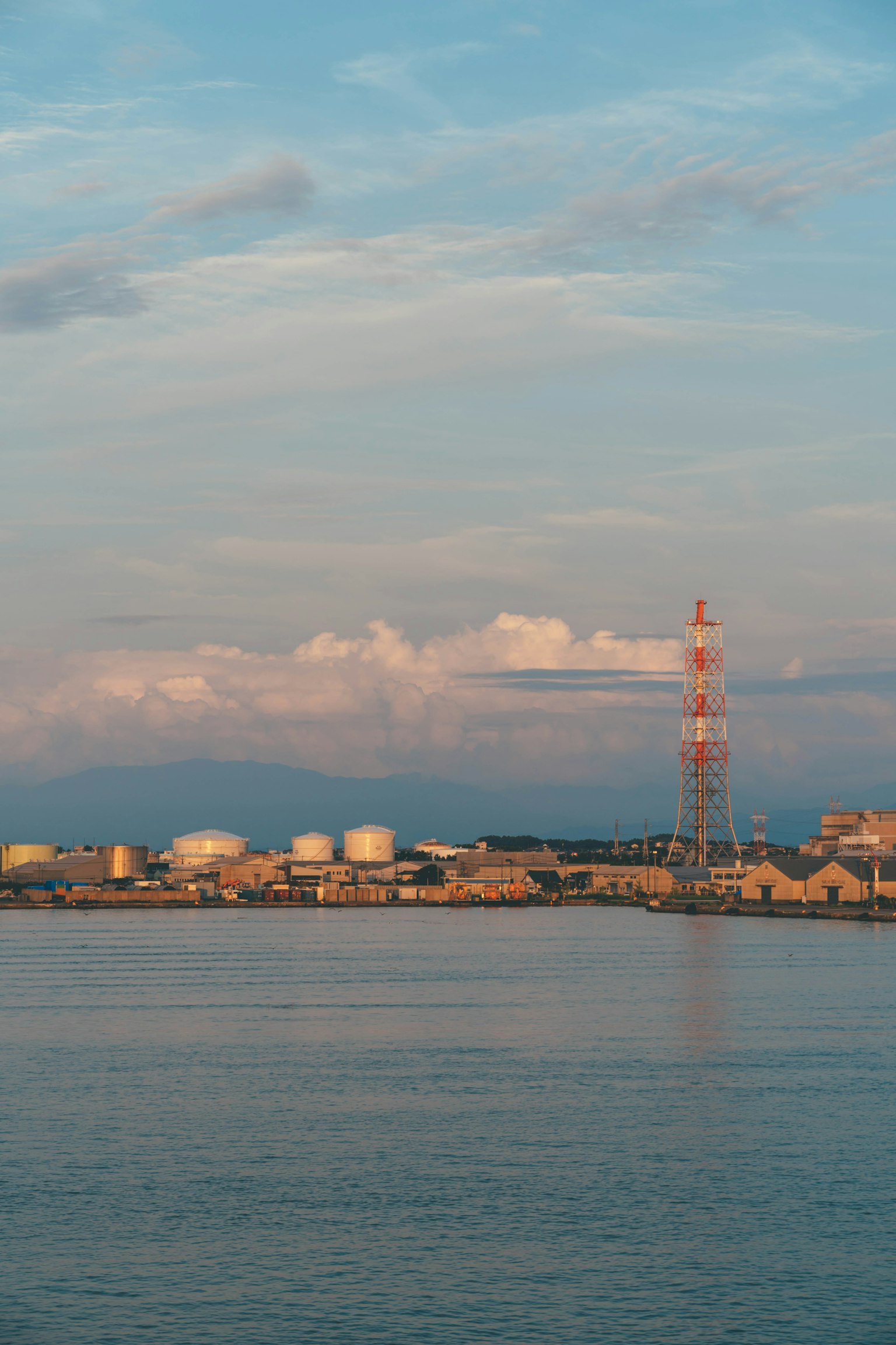 Industrielandschaft mit Kommunikationsturm und Lagertanks vor blauem Meer und Himmel
