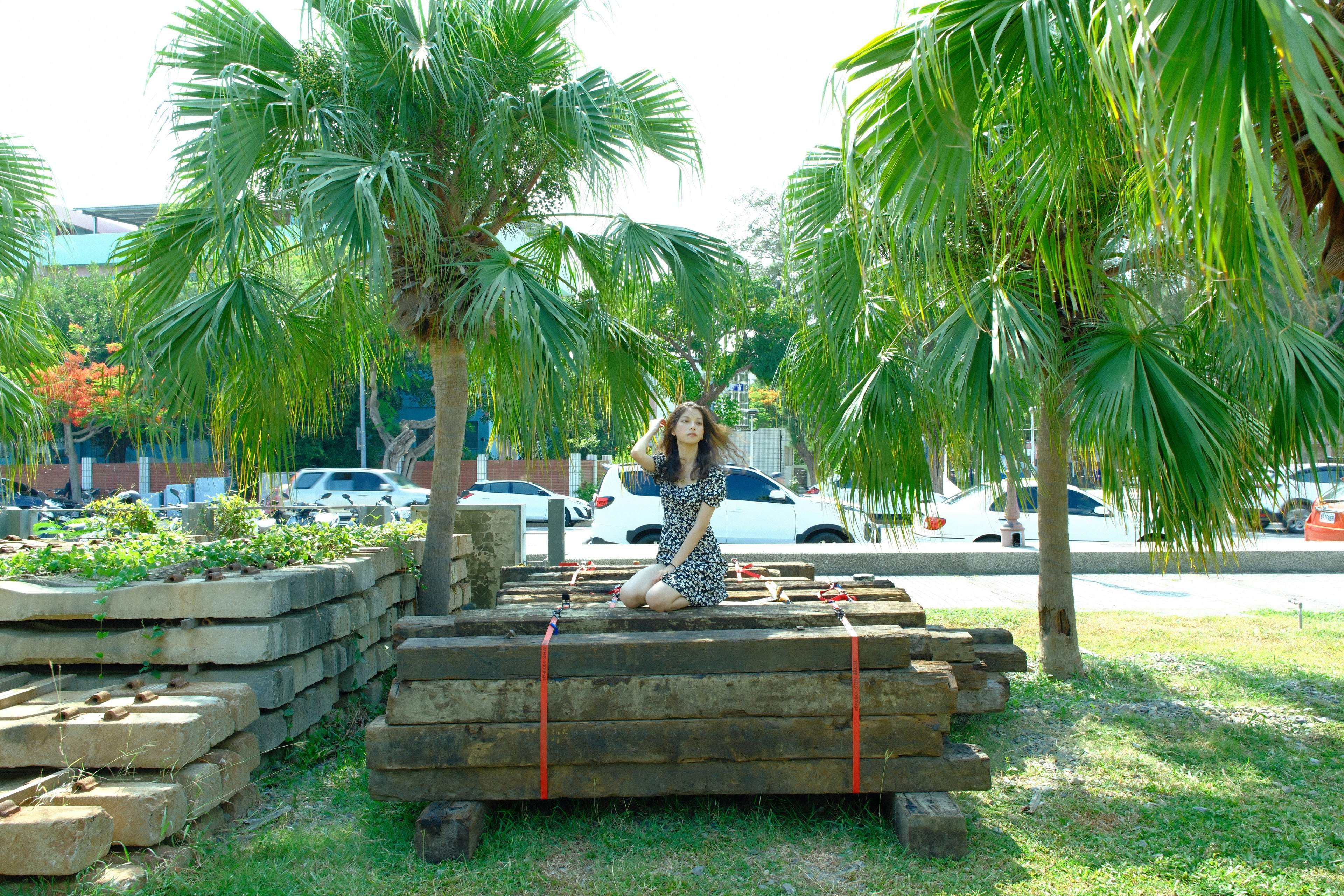woman sitting on a bench outdoors on a lawn with palm trees