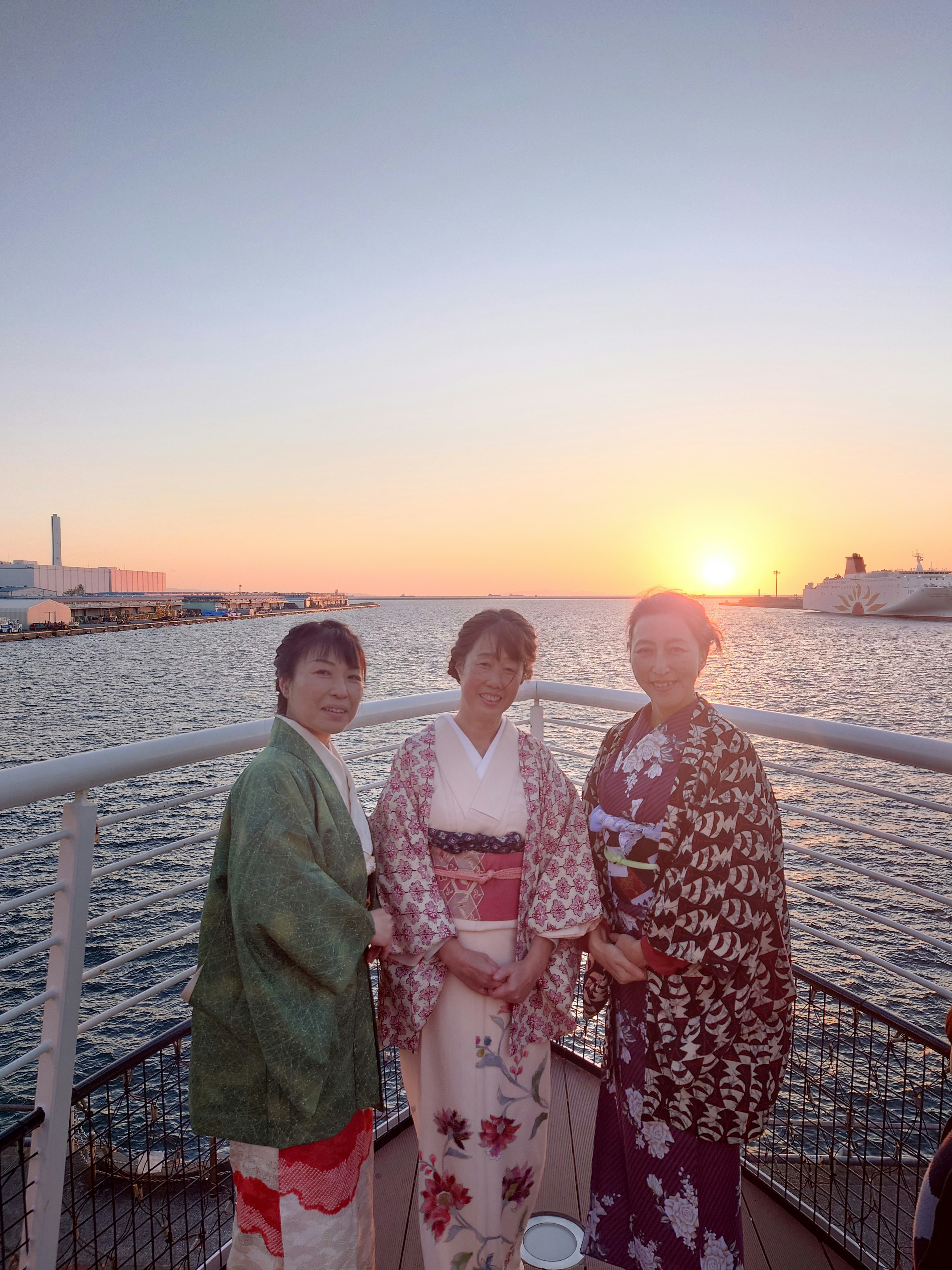 夕暮れの川沿いで着物姿の3人が並ぶ船上