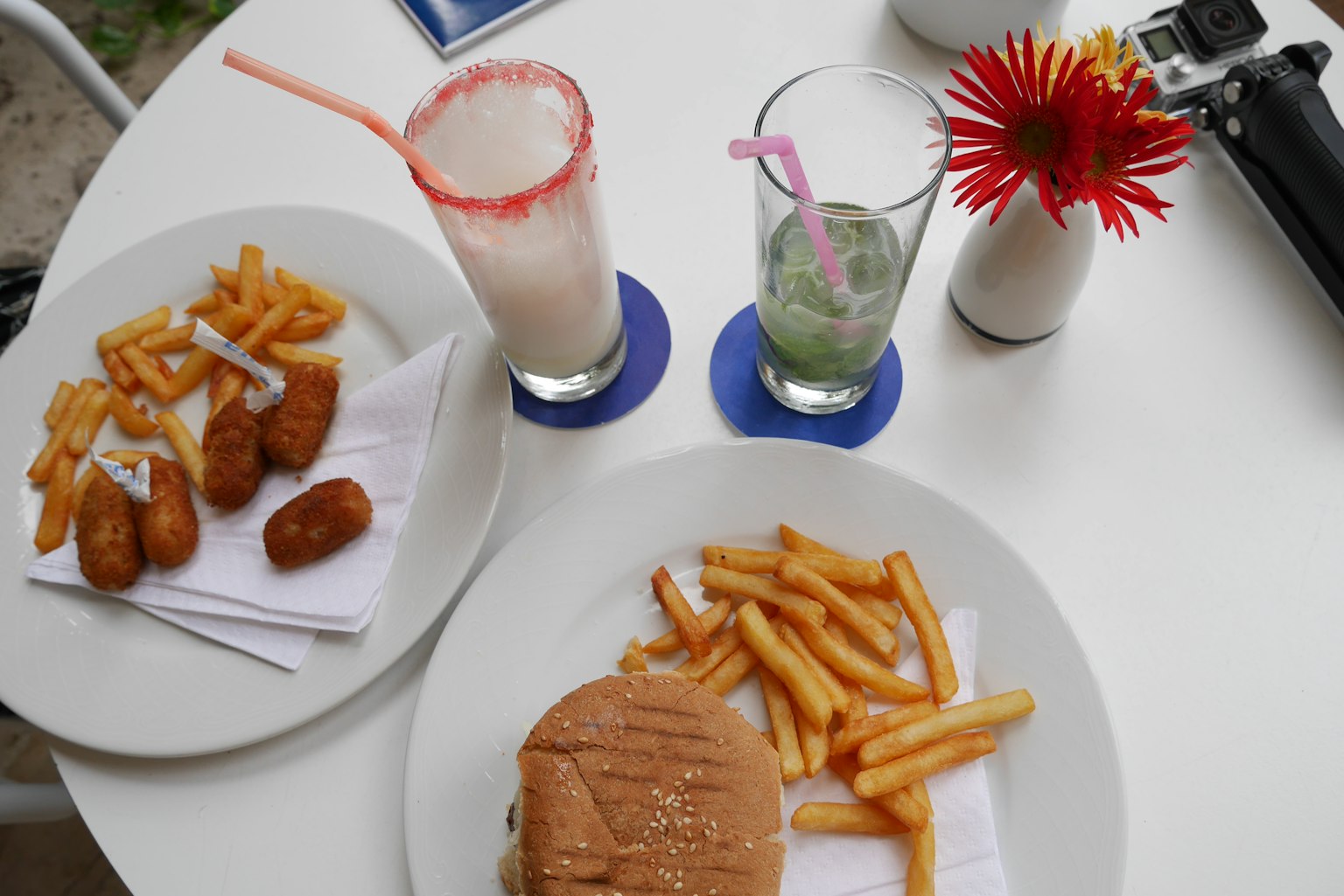 Une table avec un hamburger et des frites accompagnés de deux boissons colorées