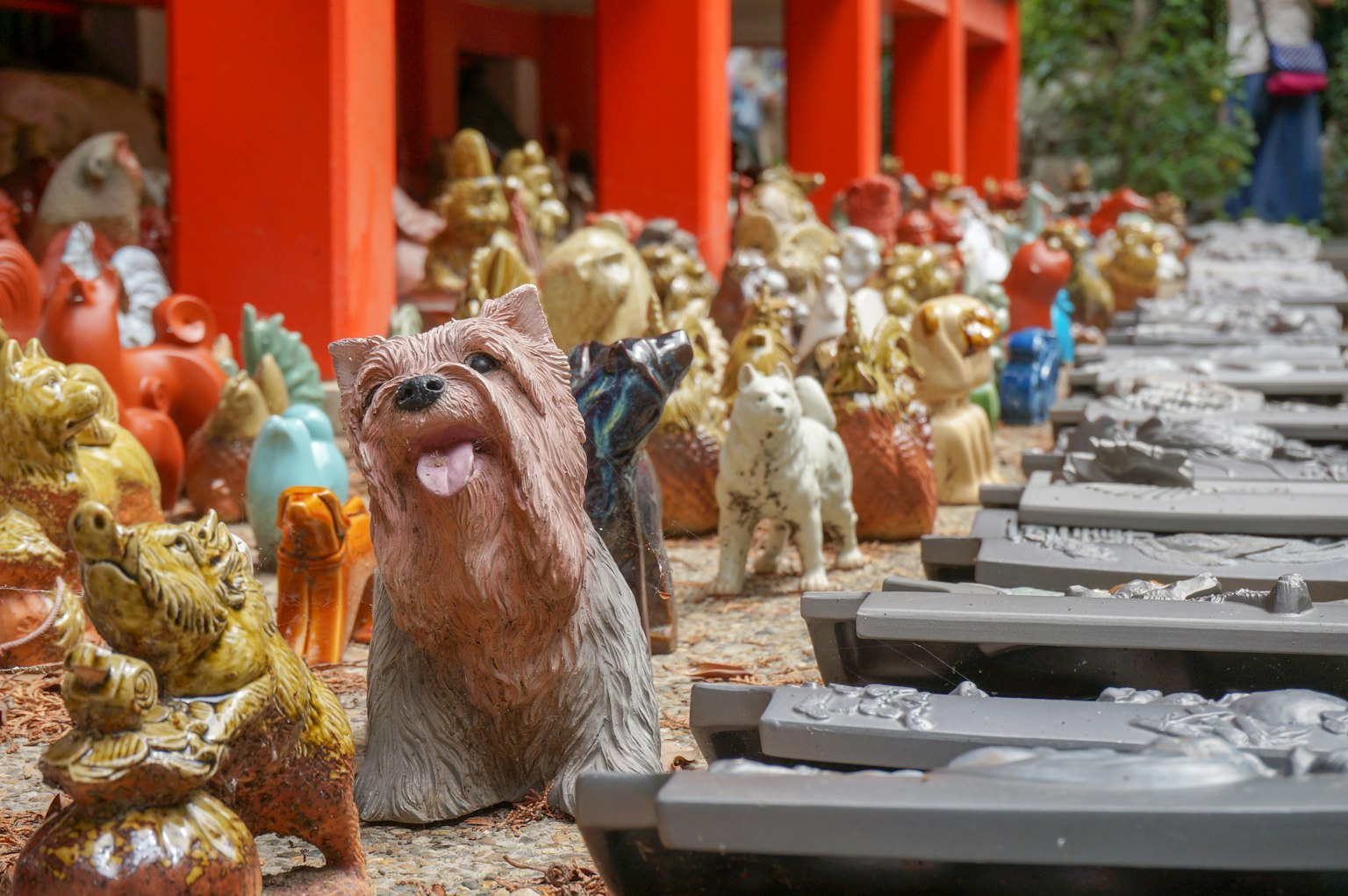 Animales de cerámica coloridos exhibidos con una estatua de perro central y pilares naranjas al fondo