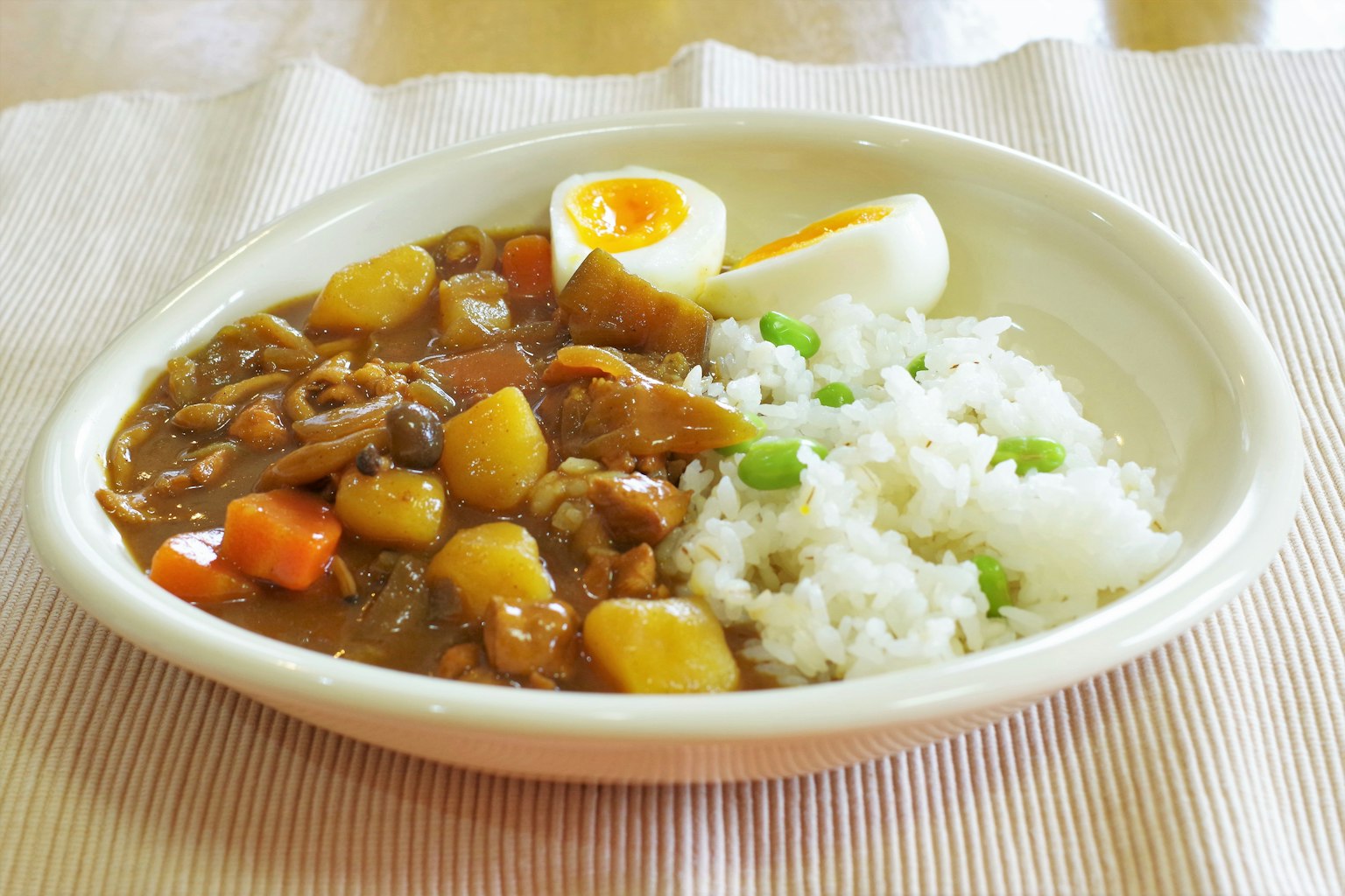 Un plato de curry con verduras acompañado de arroz blanco y un huevo cocido a la mitad