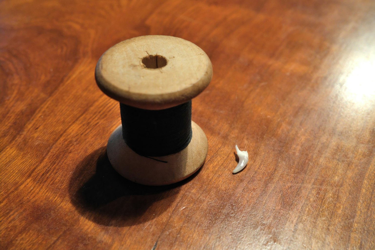 A wooden spool with black thread and a small white piece on a wooden table