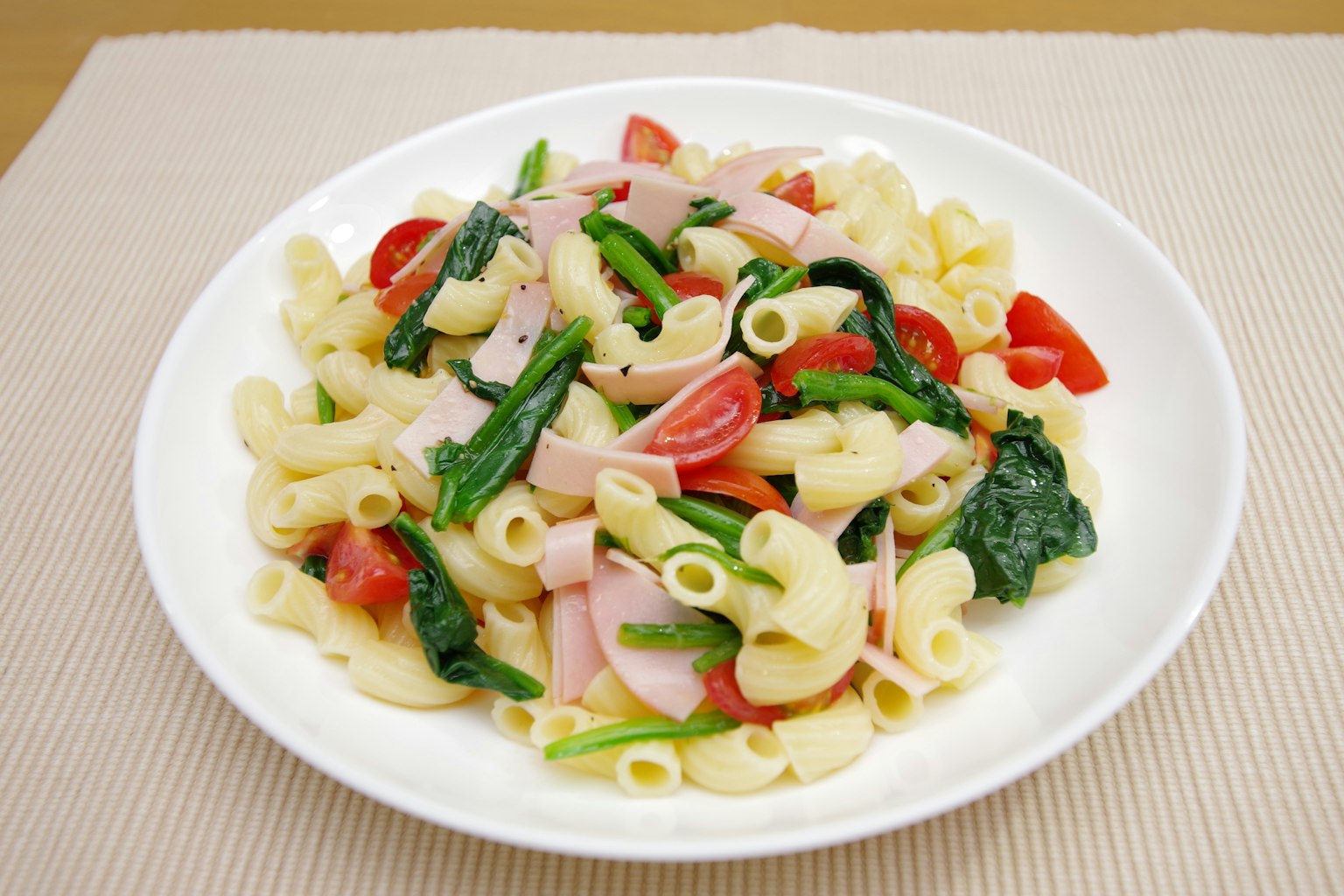 Cremiger Nudelsalat mit Tomaten und Spinat in einer weißen Schüssel