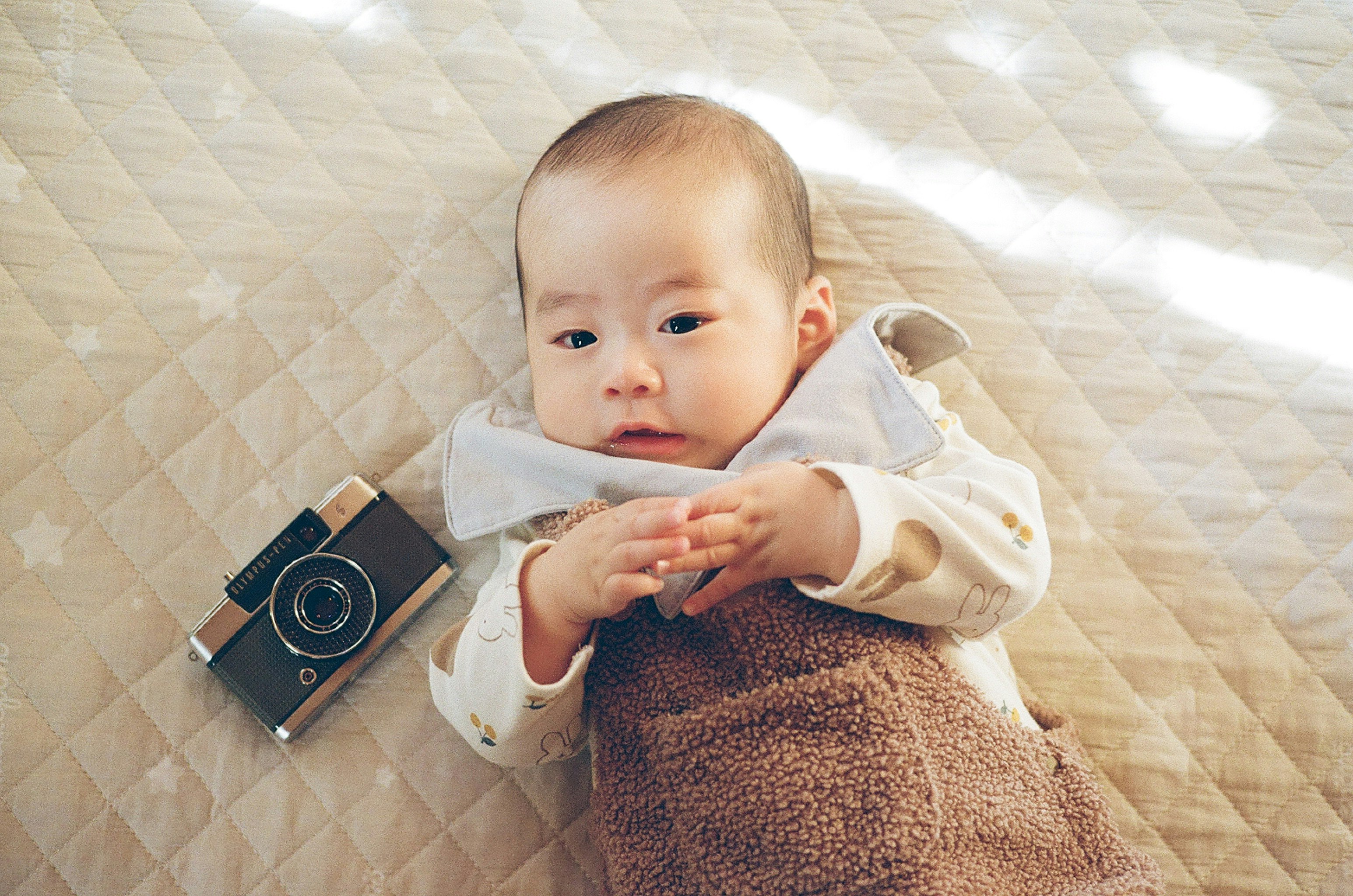 baby lying on a quilt with a small camera prop