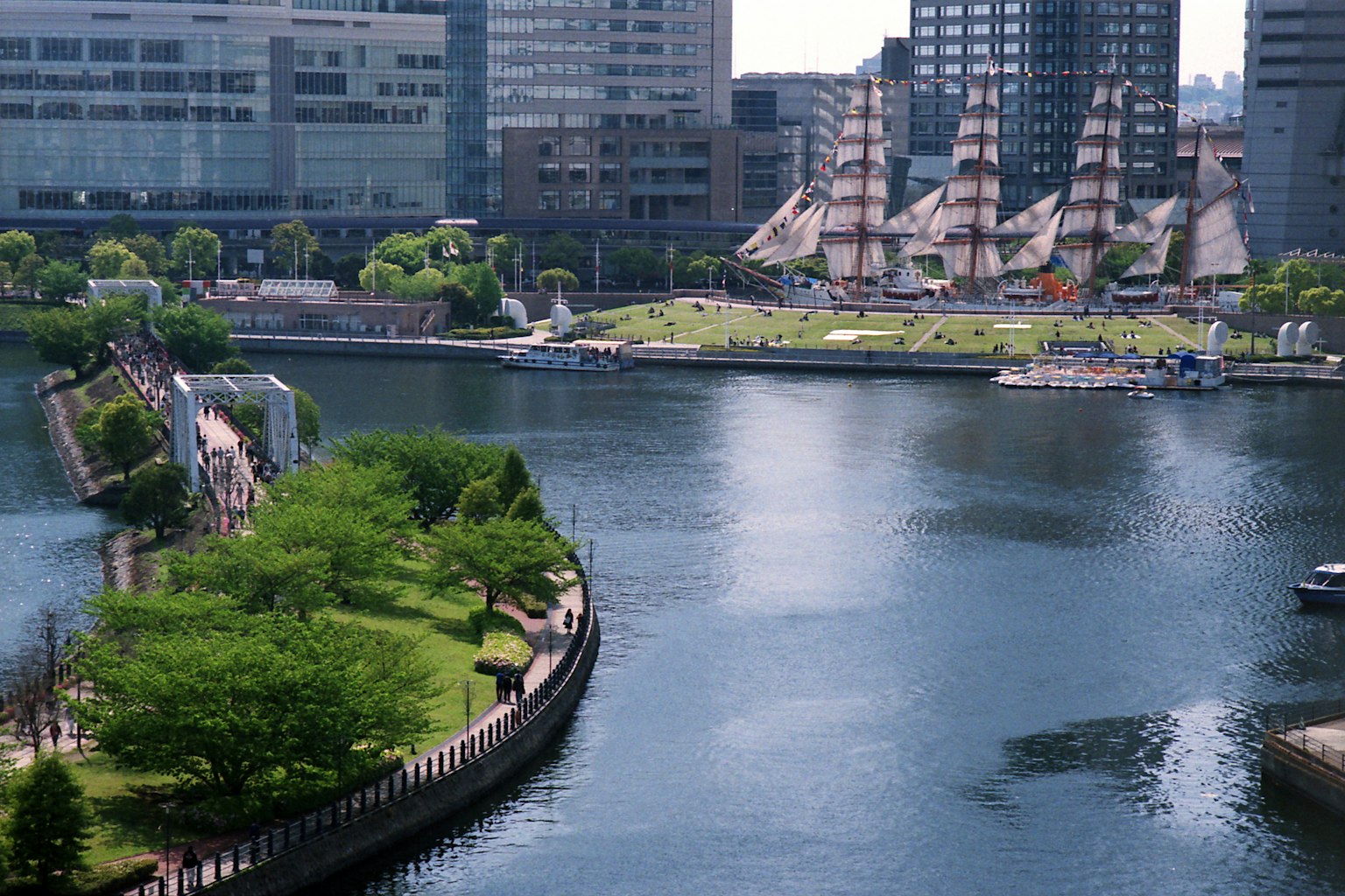 Modern urban landscape with a calm river featuring boats and green parks