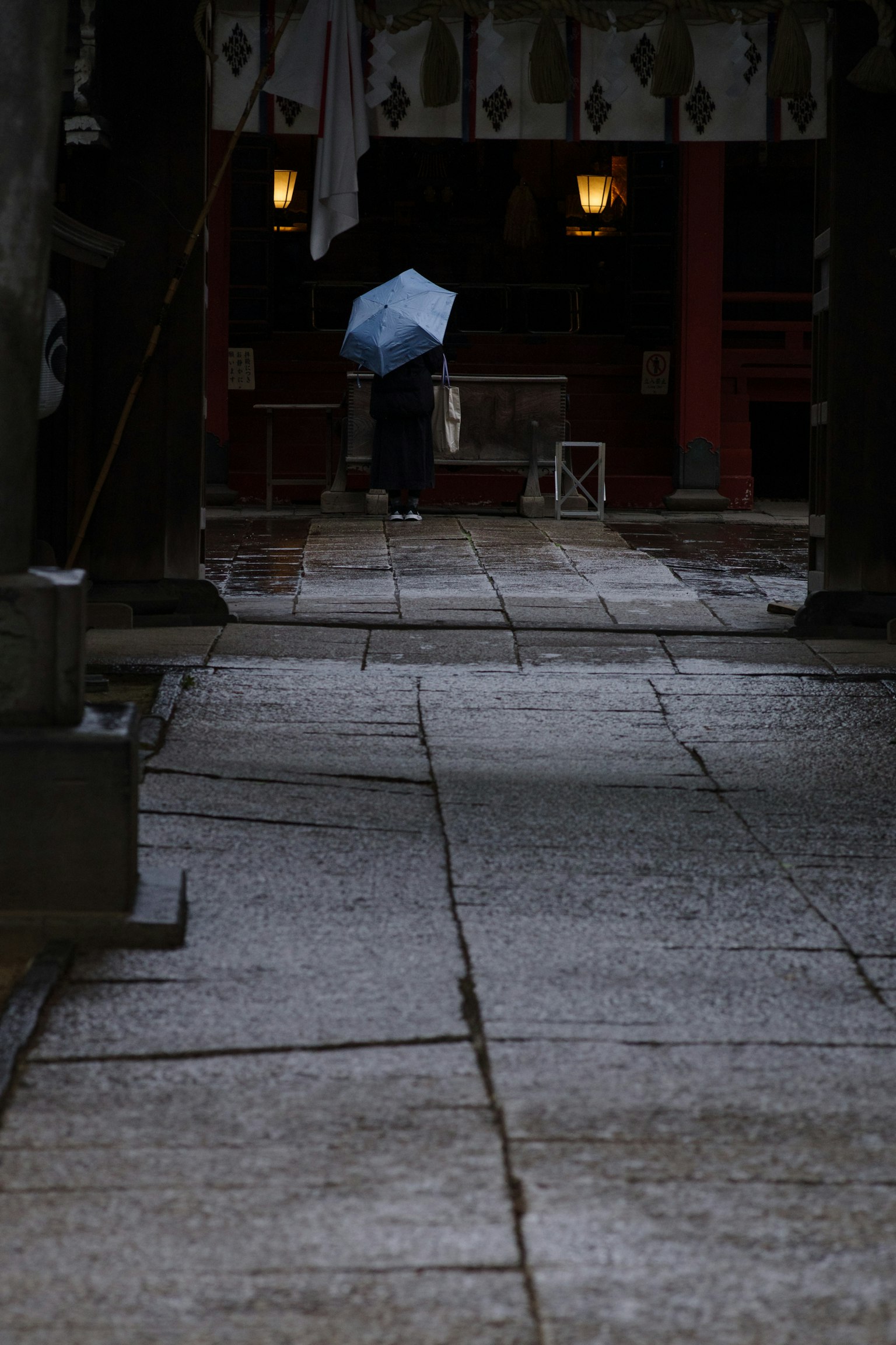 Eine Person mit einem Regenschirm, die auf einem Steinweg in einem Tempel bei Regen geht