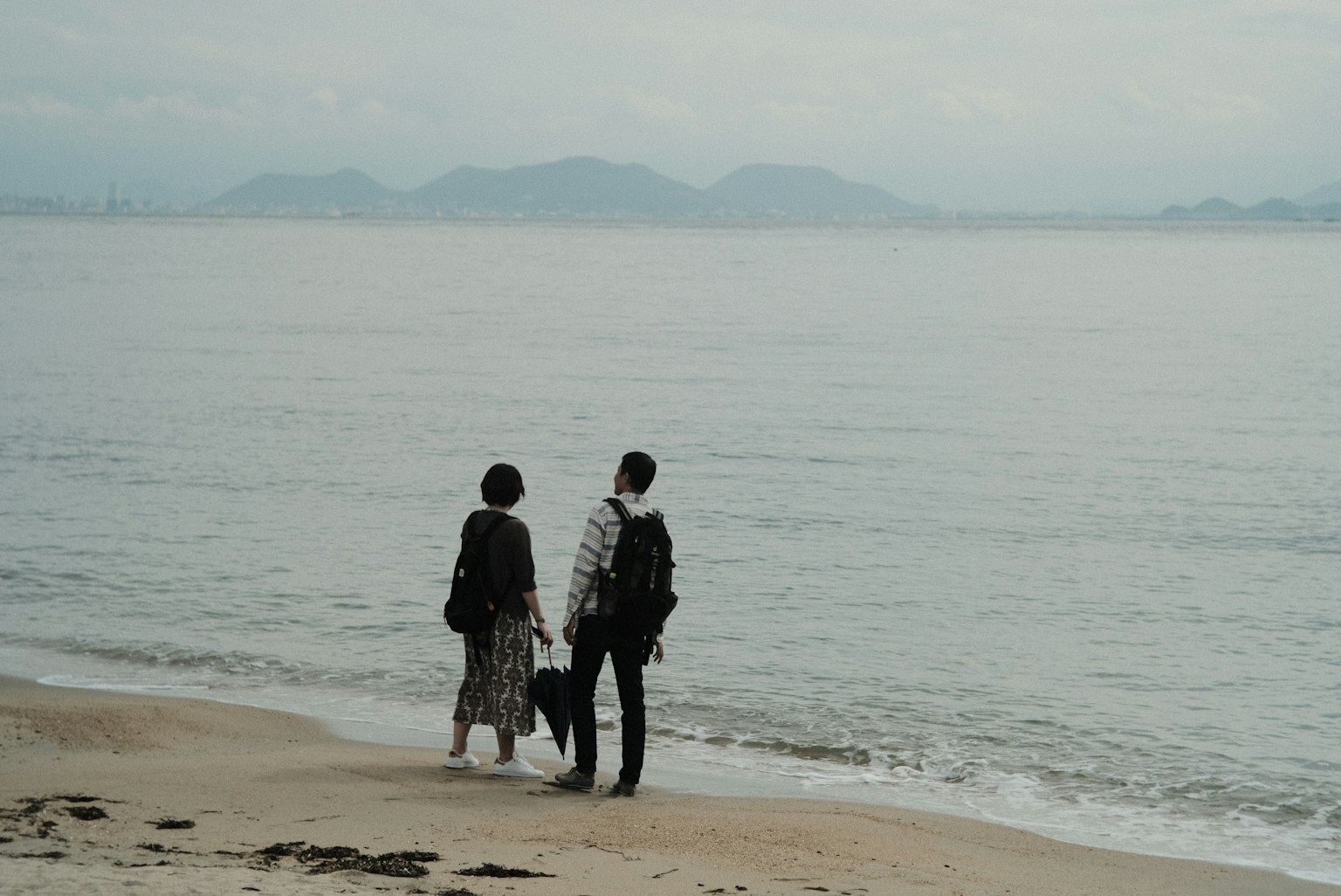 สองคนยืนอยู่บนชายหาดมองไปที่ทะเลที่สงบ