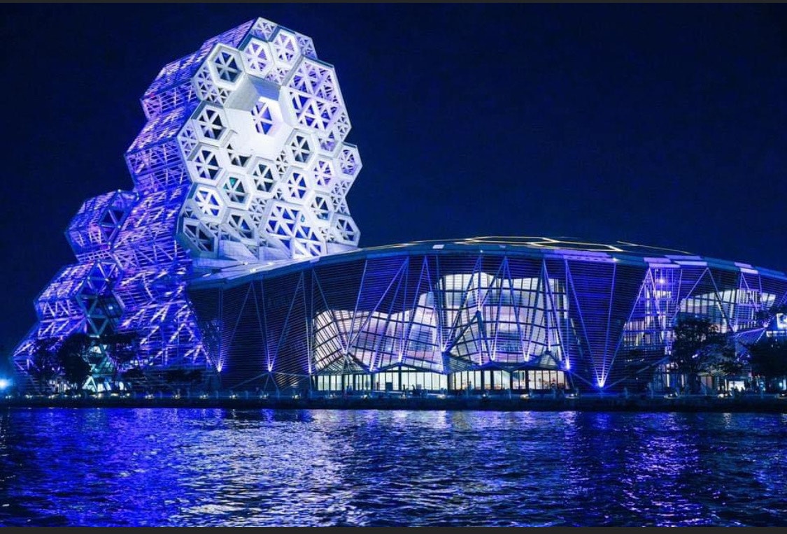 Edificio futuristico illuminato e cupola lungo un fiume di notte